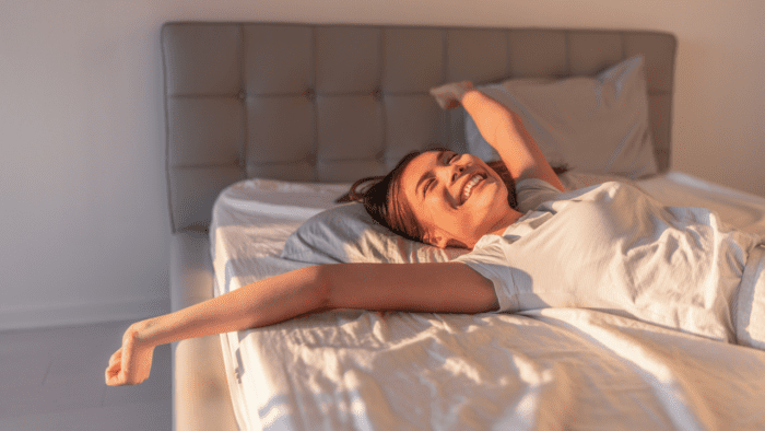 Happy woman waking up, stretching in bed with a smile after a restful sleep.