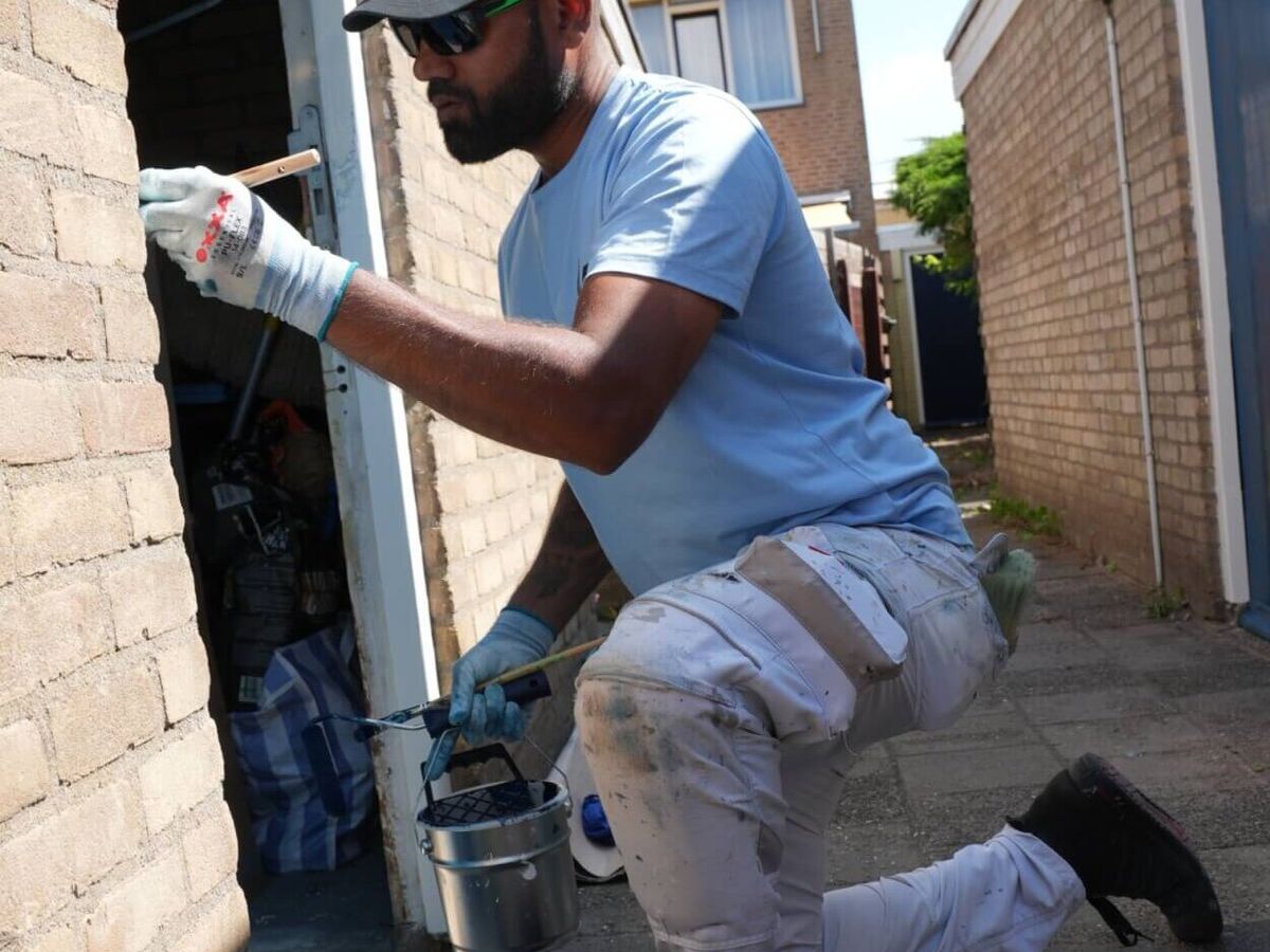 Schilder van Koestr schildert een kozijn in een bakstenen gevel