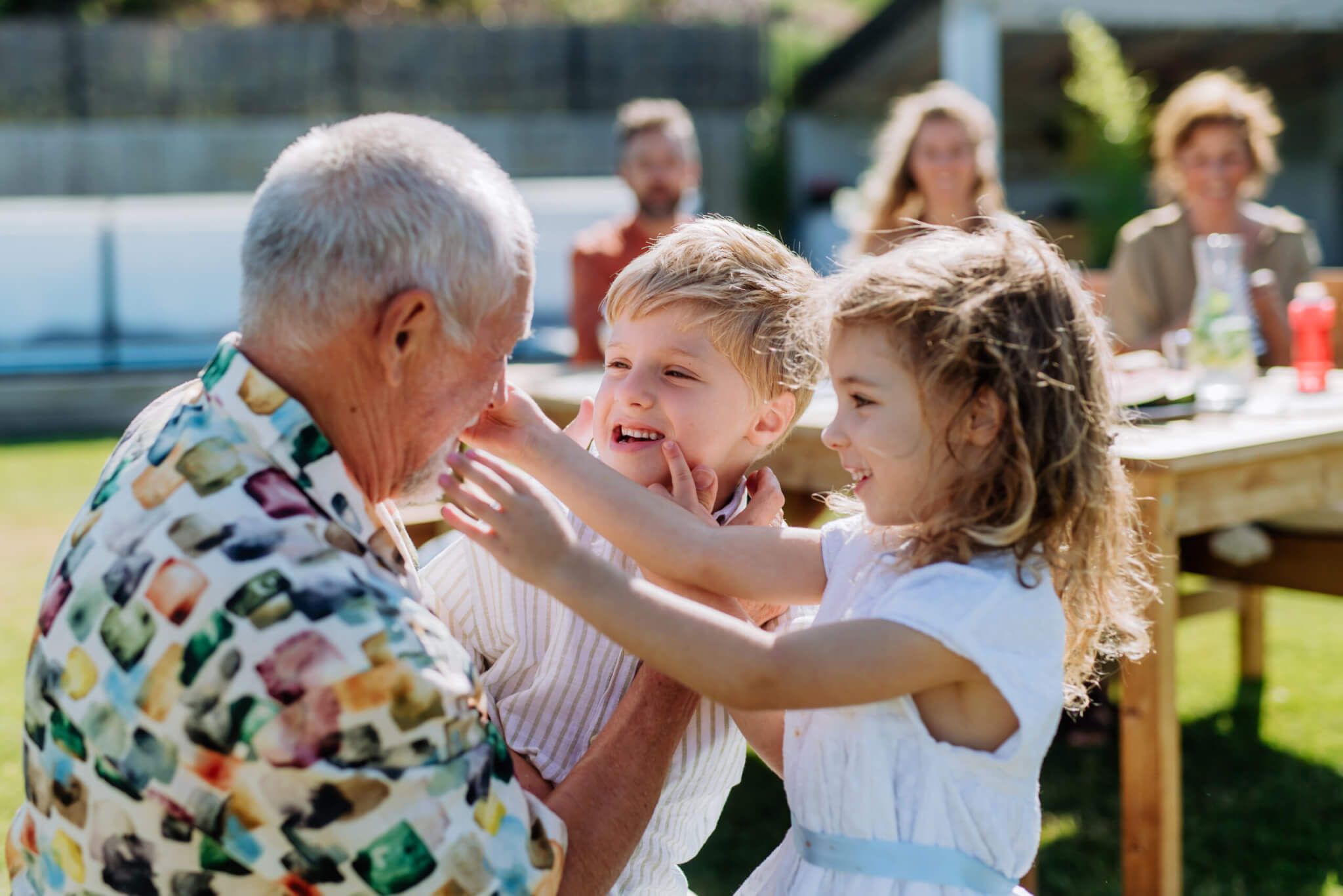 Een opa speelt lachend met zijn twee kleinkinderen in de tuin