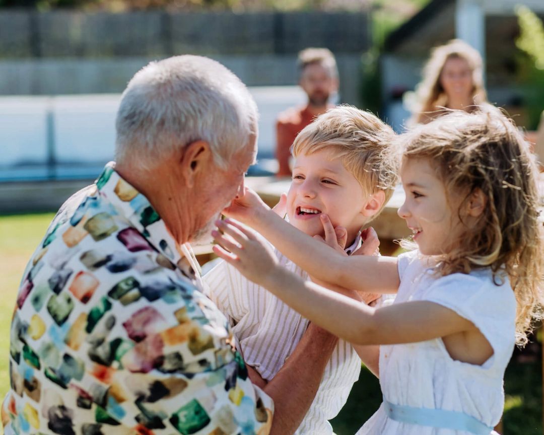 Een opa speelt lachend met zijn twee kleinkinderen in de tuin