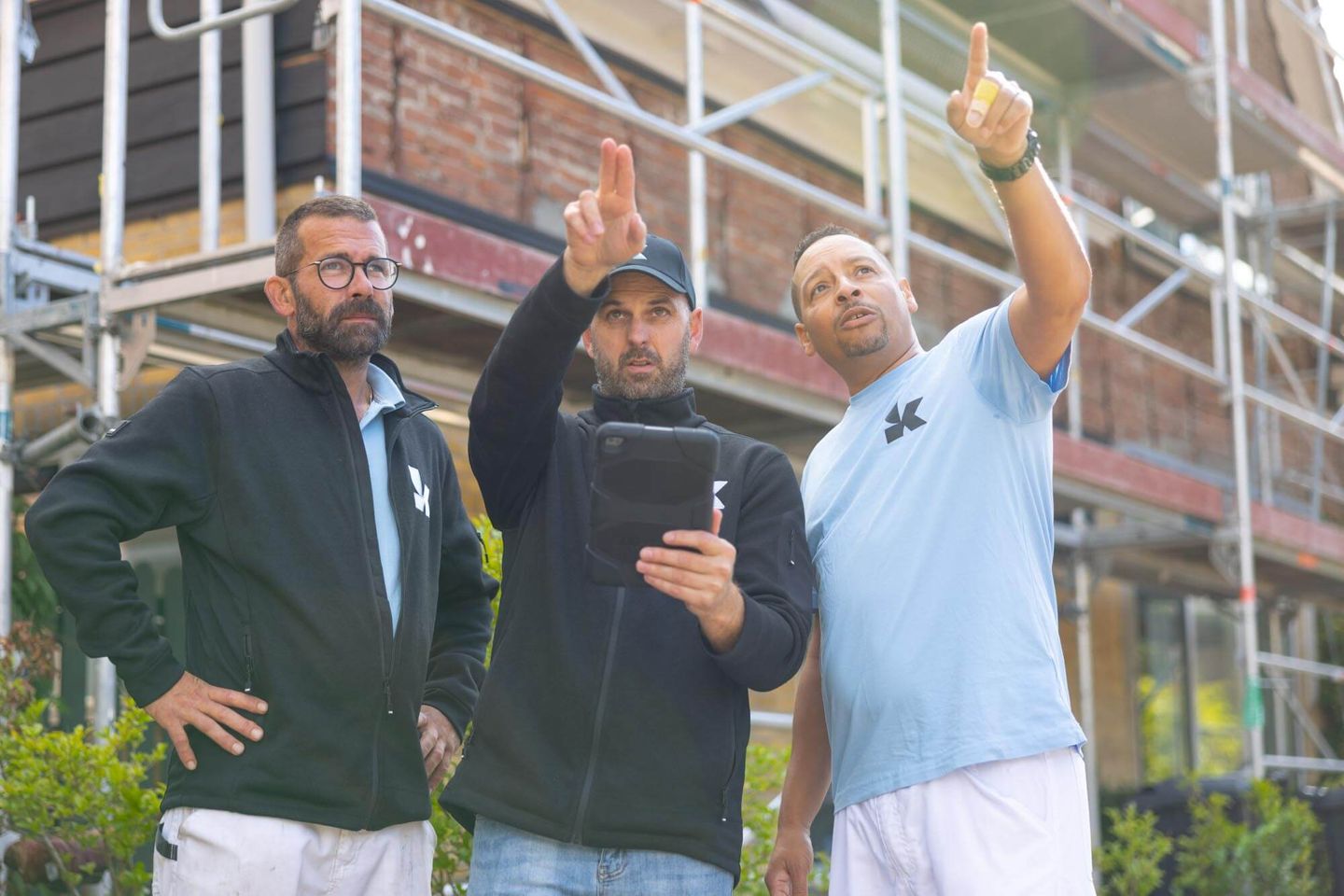 Drie vakmensen van Koestr overleggen bij een woning in de steigers
