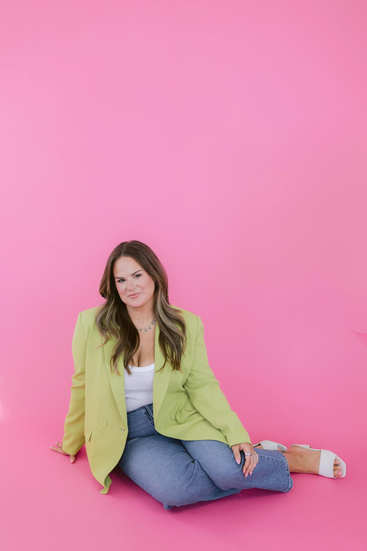 Candace sitting cross-legged on the floor against a hot pink backdrop