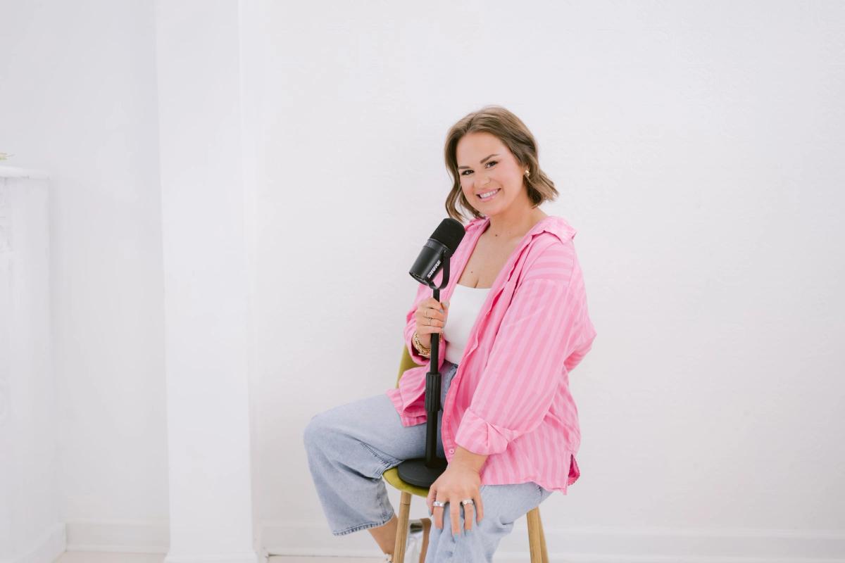 Candace laughing behind a podcast microphone in a pink striped shirt