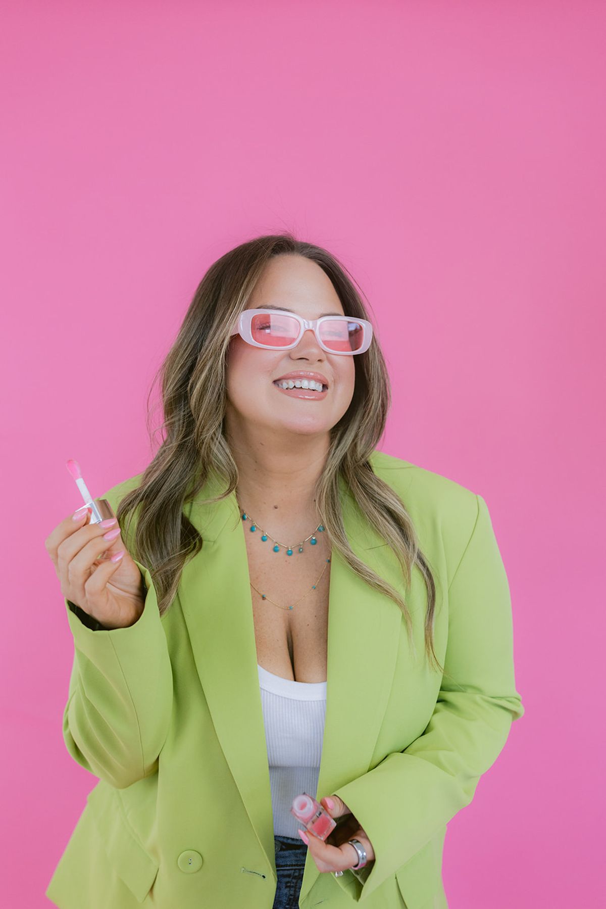 Candace in front of a pink background holding makeup and smiling