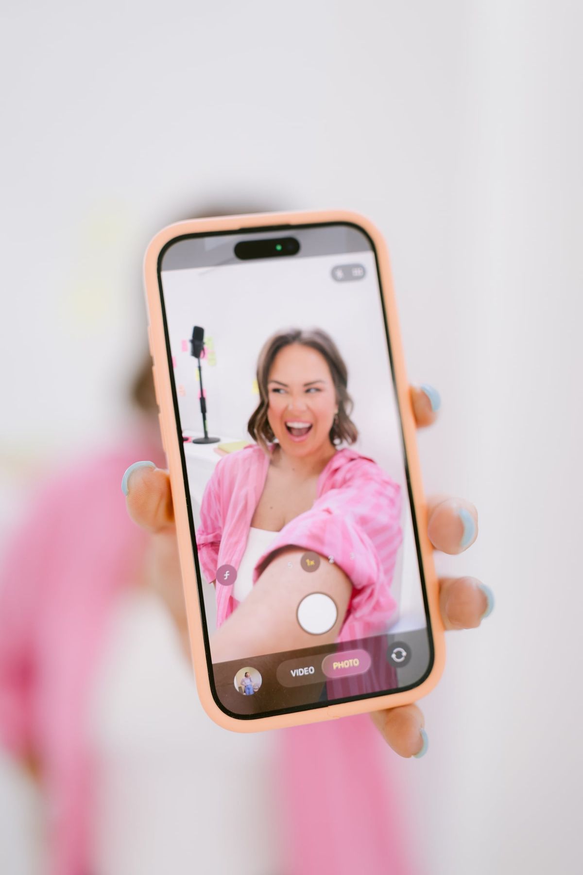 Candace holding her phone up to the camera, filming herself in a pink striped shirt