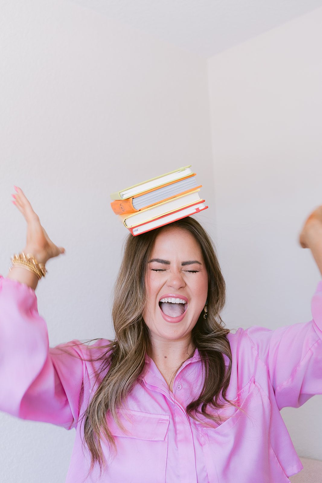 Candace laughing with a stack of books balanced on her head and her arms in the air