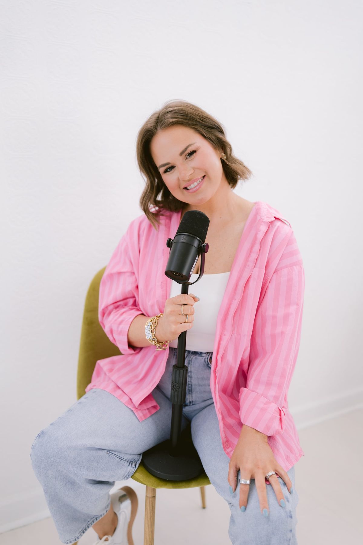 Candace seated with a podcast microphone, in a pink striped shirt