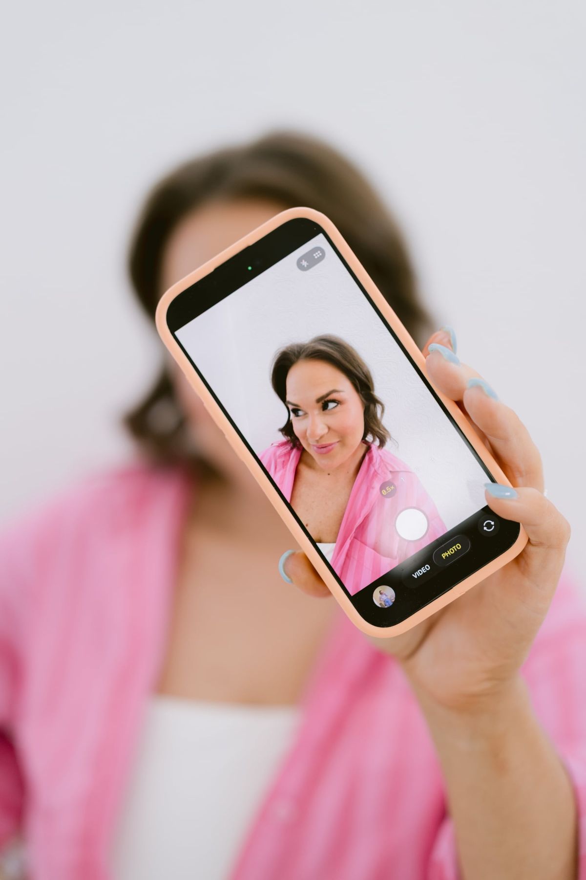 Candace holding up her phone, mid-laugh, in a pink striped shirt