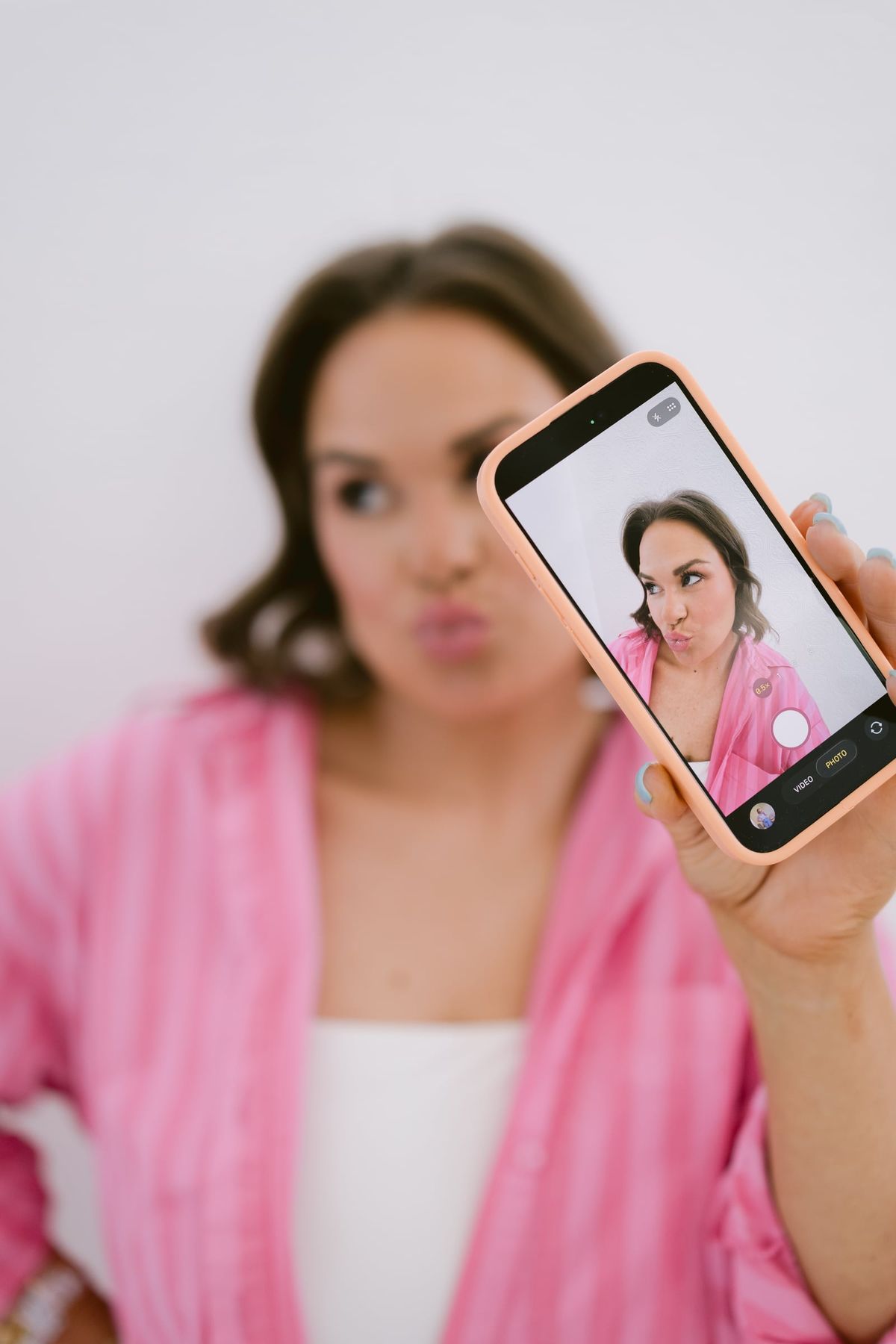 Candace pulling a face at her phone camera, filming herself in a pink striped shirt