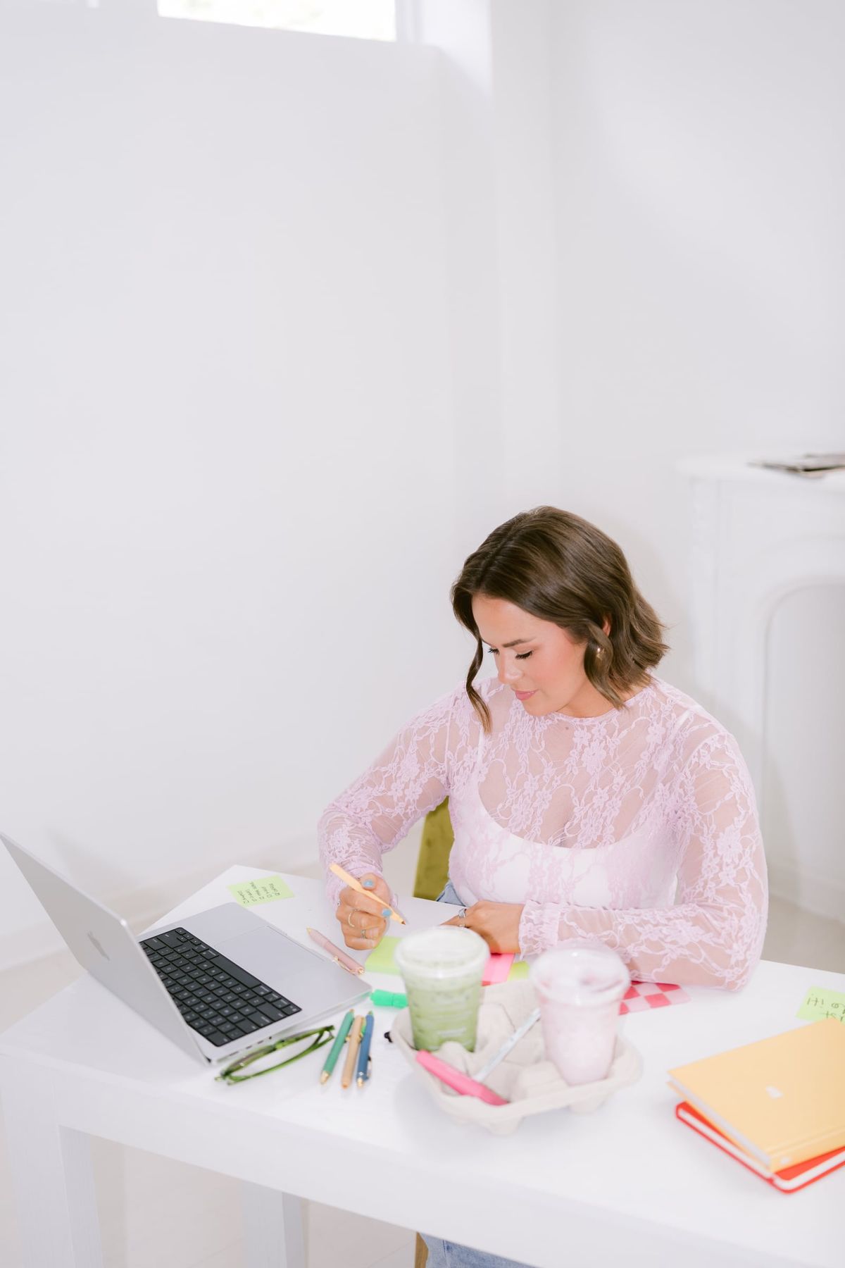 Candace working at a white desk with her laptop, notebooks and an iced matcha