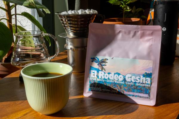 a cup of coffee next to a bag of El Rodeo Gesha, in pink packaging