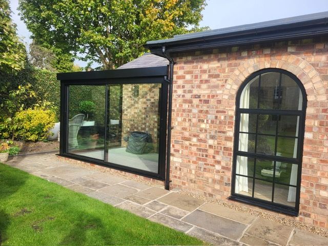 Glass box beside an arched steel-look window on a brick home in Bowdon