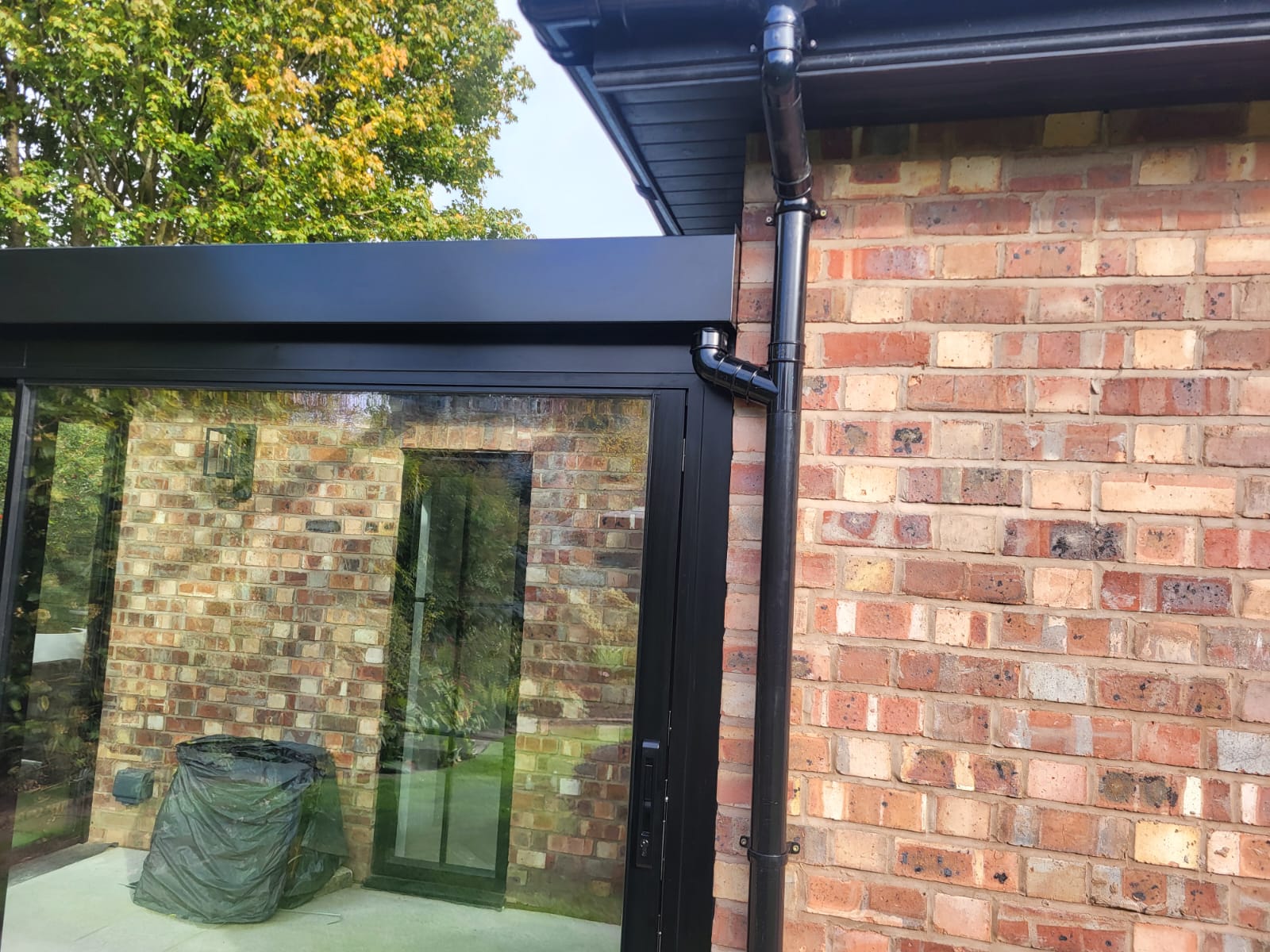 Black fascia and downpipe meeting a black aluminium glass box frame against brick