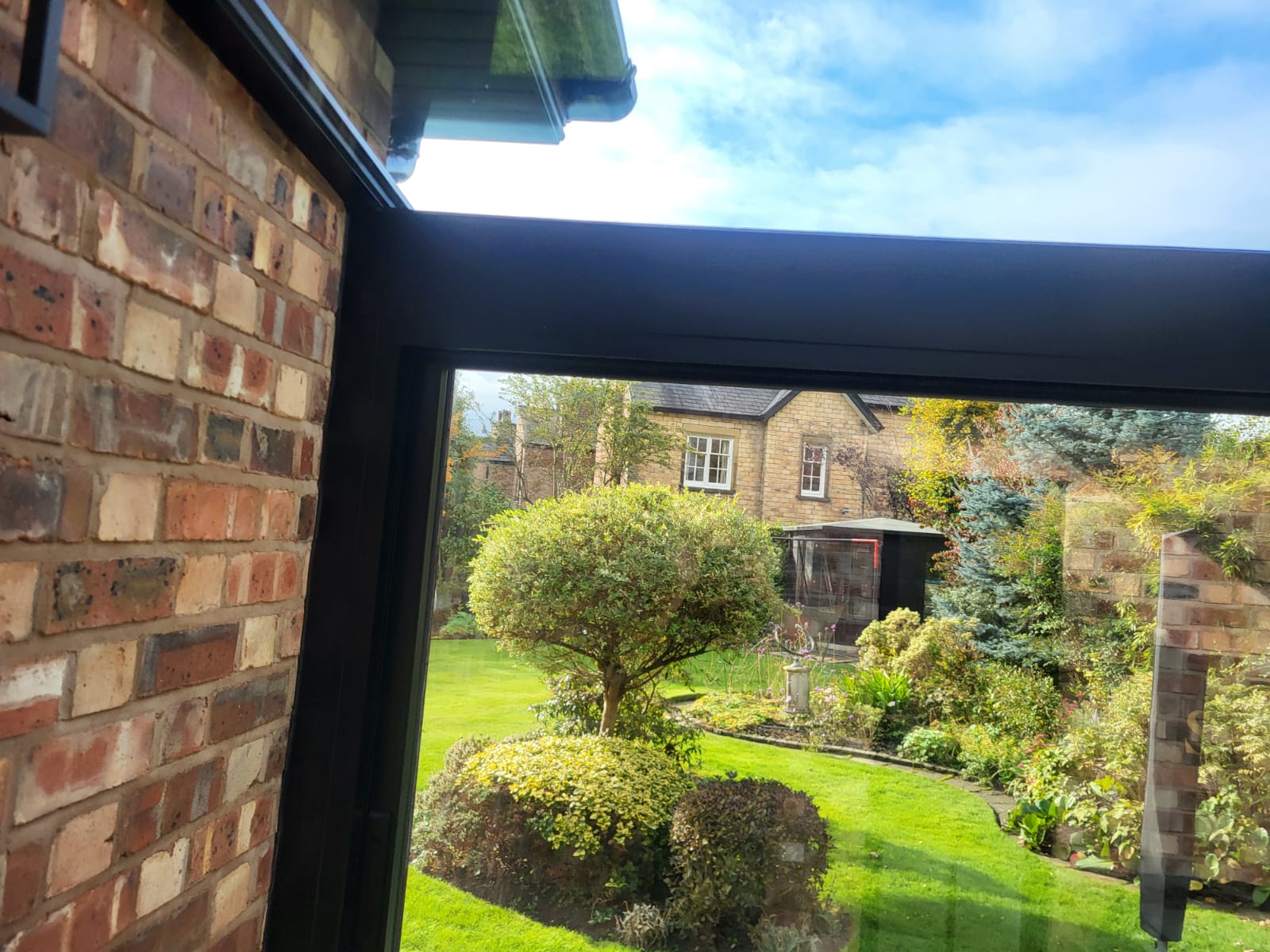 View of a mature Cheshire garden through the corner glazing of a glass box