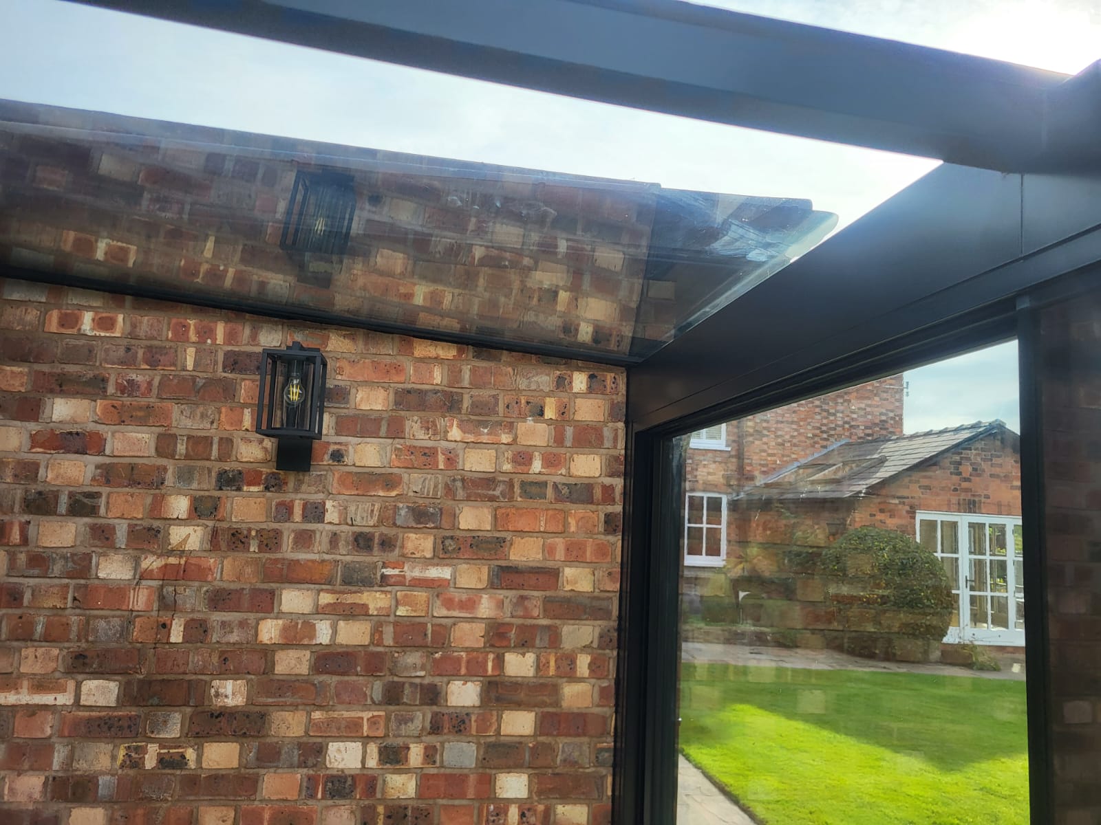 Glass roof meeting a brick wall with a black wall lantern, inside a glass box