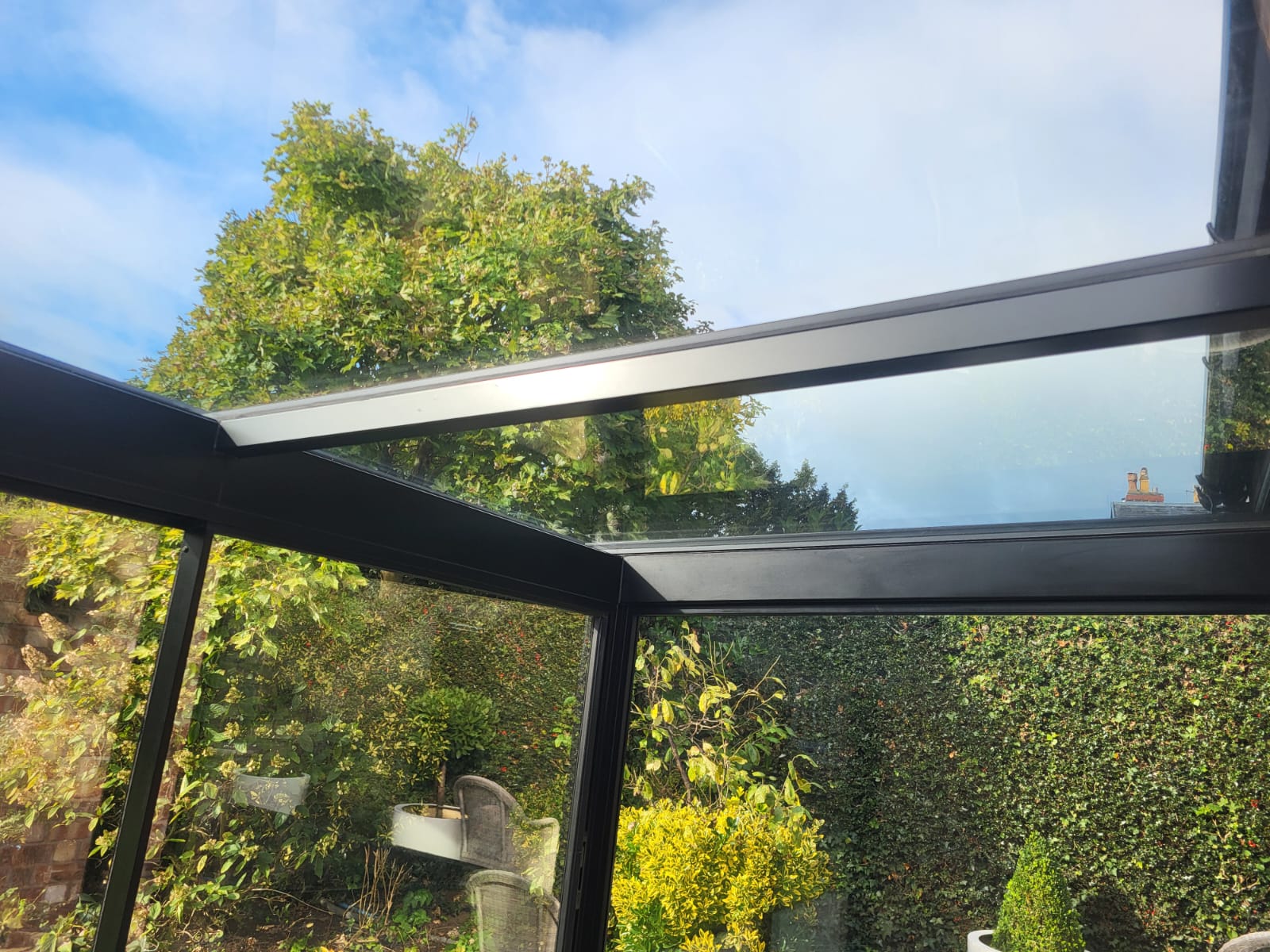 Looking up through the glass roof and black aluminium rafters of a glass box