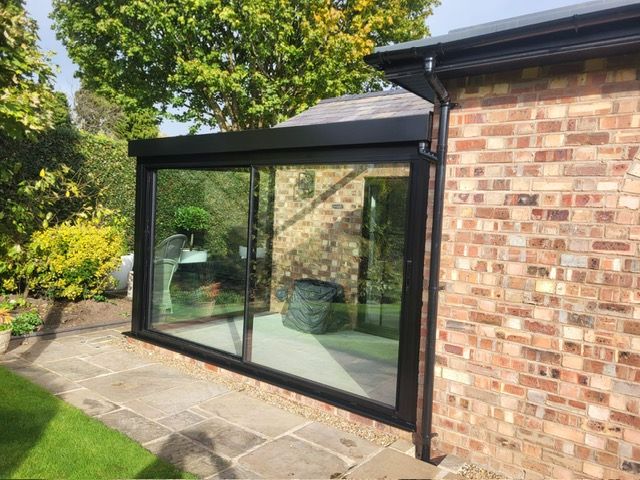 Side view of a black aluminium glass box with sliding doors on a Cheshire patio