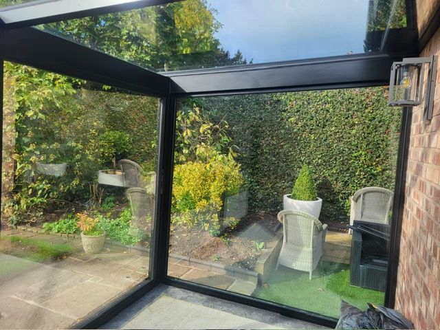 Inside a black-framed glass box looking out across a garden terrace