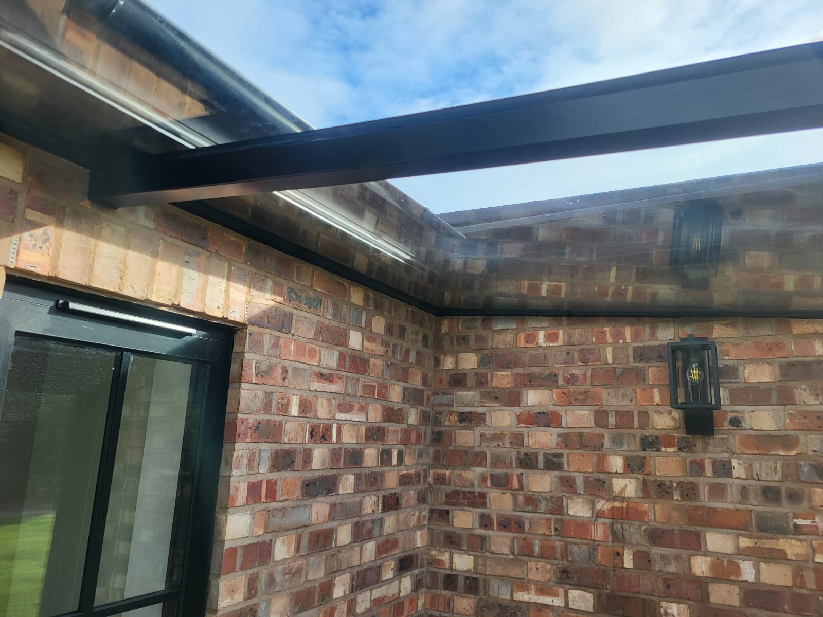 Glass roof junction with brick wall and black guttering on a Bowdon glass box