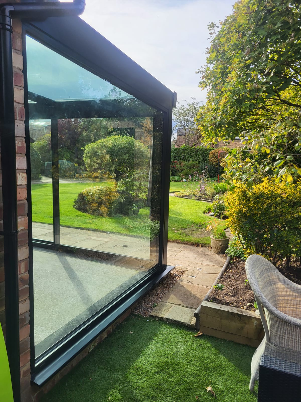 Glass corner and sloping glass roof of a black-framed glass box with garden beyond