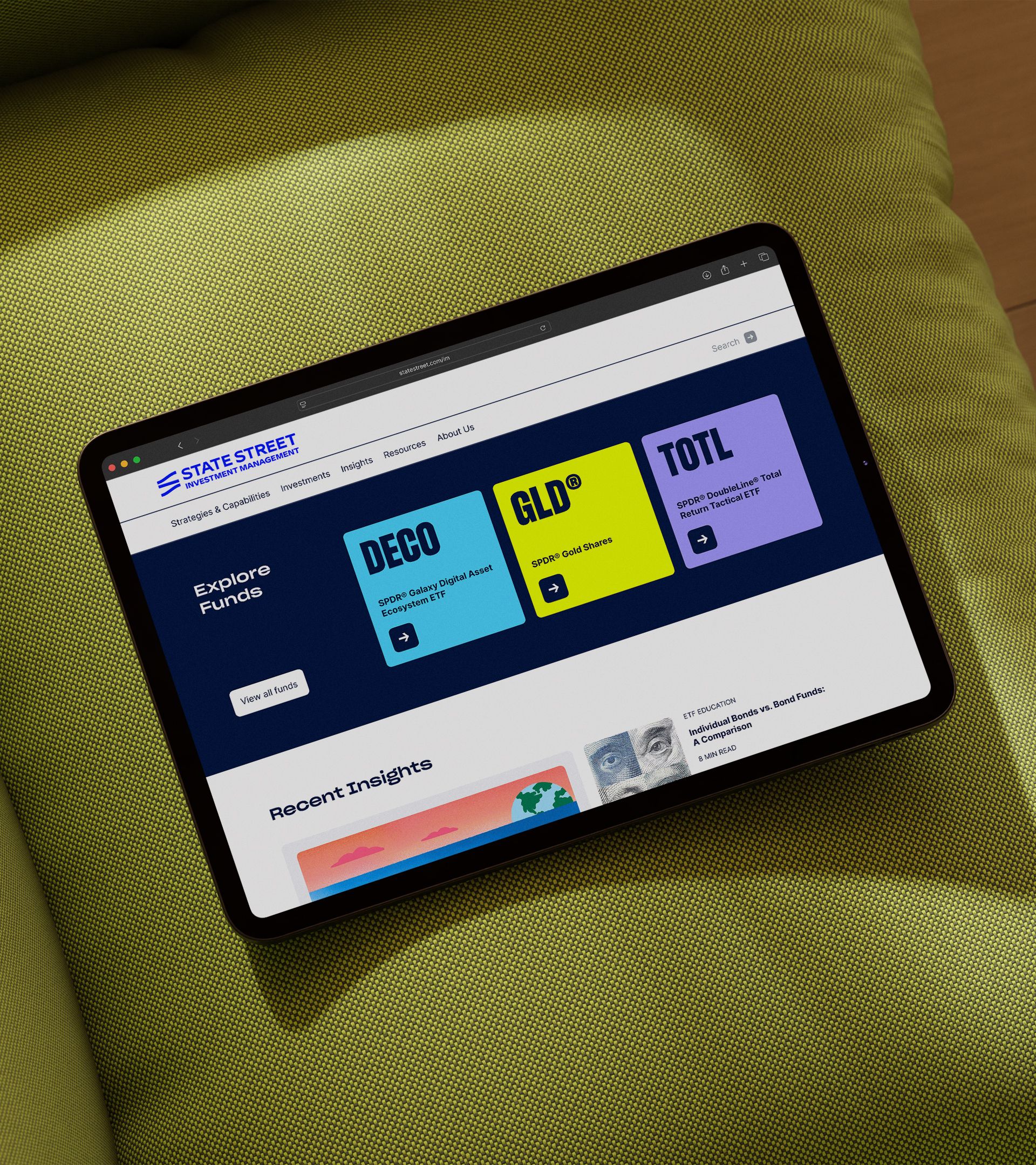 iPad on chartreuse fabric displaying SSIM website "Explore Funds" section with DECO, GLD, and TOTL fund tiles in bold color blocks