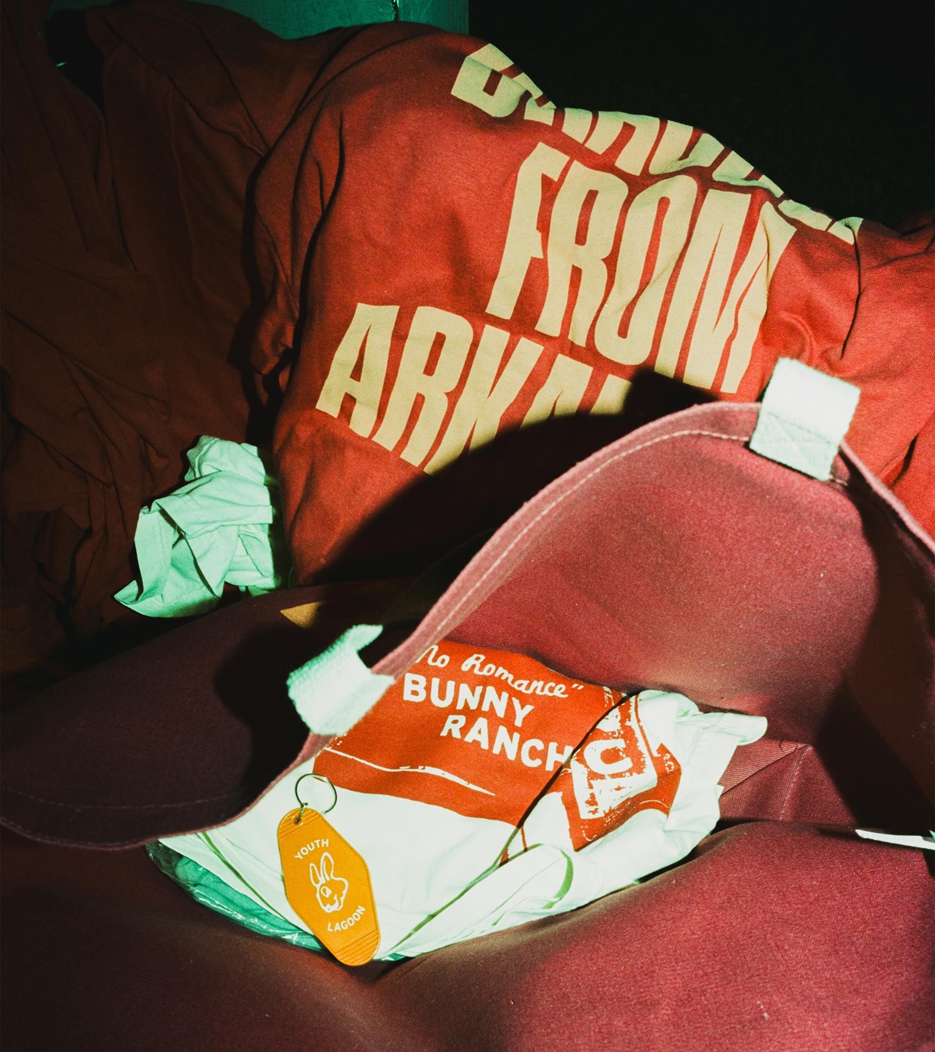 Youth Lagoon RDID merch pile: red 'Dracula From Arkansas' crewneck, 'No Romance / Bunny Ranch' bag, yellow keychain