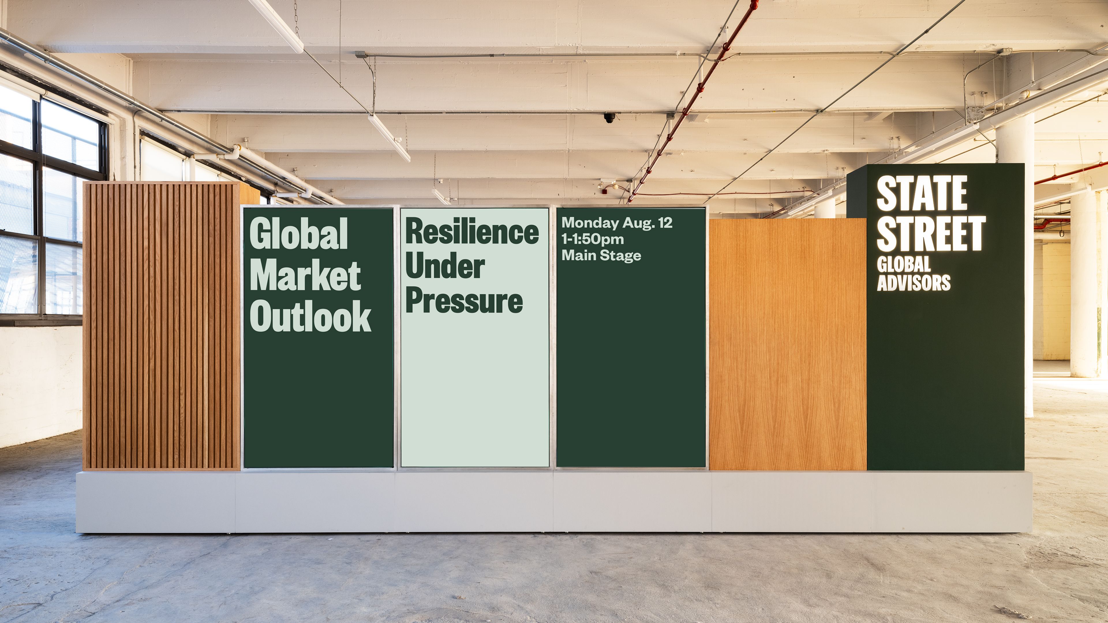 Booth rear: SSGA signage wall with fluted oak panels and framed type: "Global Market Outlook," "Resilience Under Pressure," session info