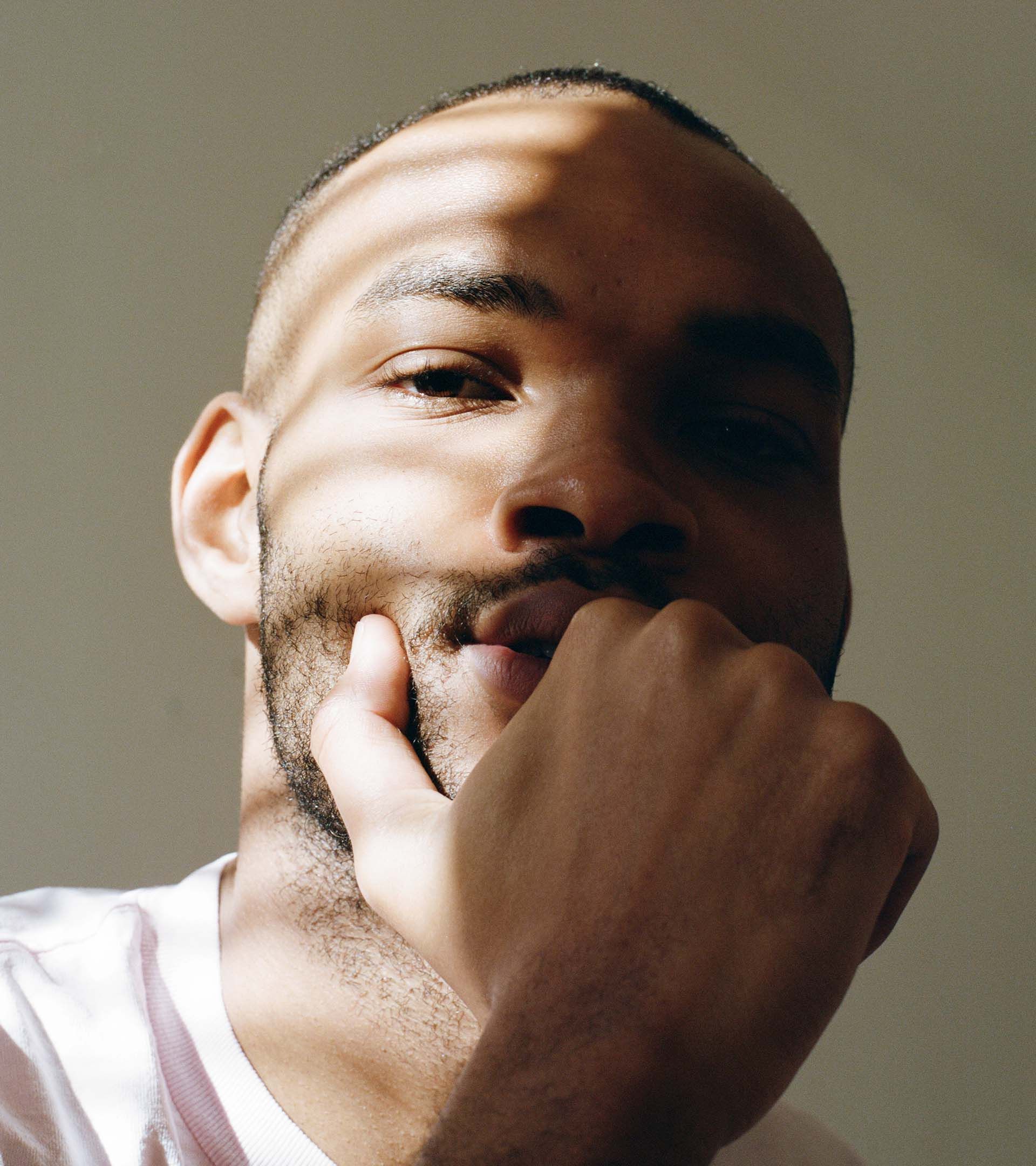 Close portrait of young man resting chin on fist, looking upward, natural directional light on warm gray background