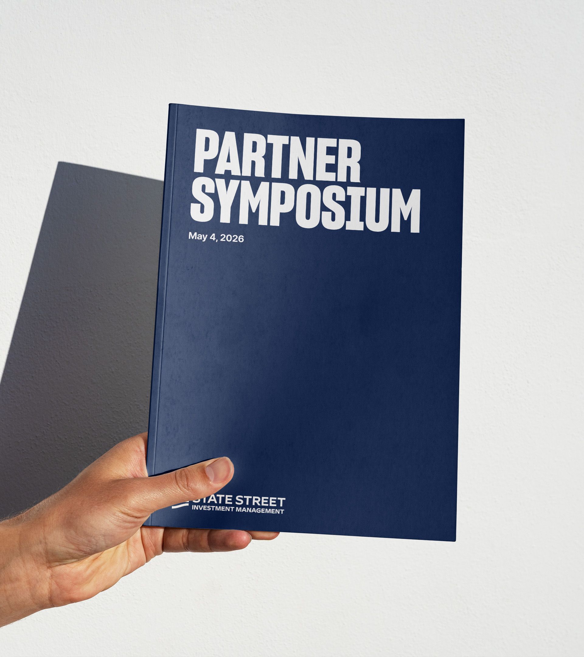 Events system application: Hand holding navy booklet reading "Partner Symposium, May 4, 2026" wordmark below