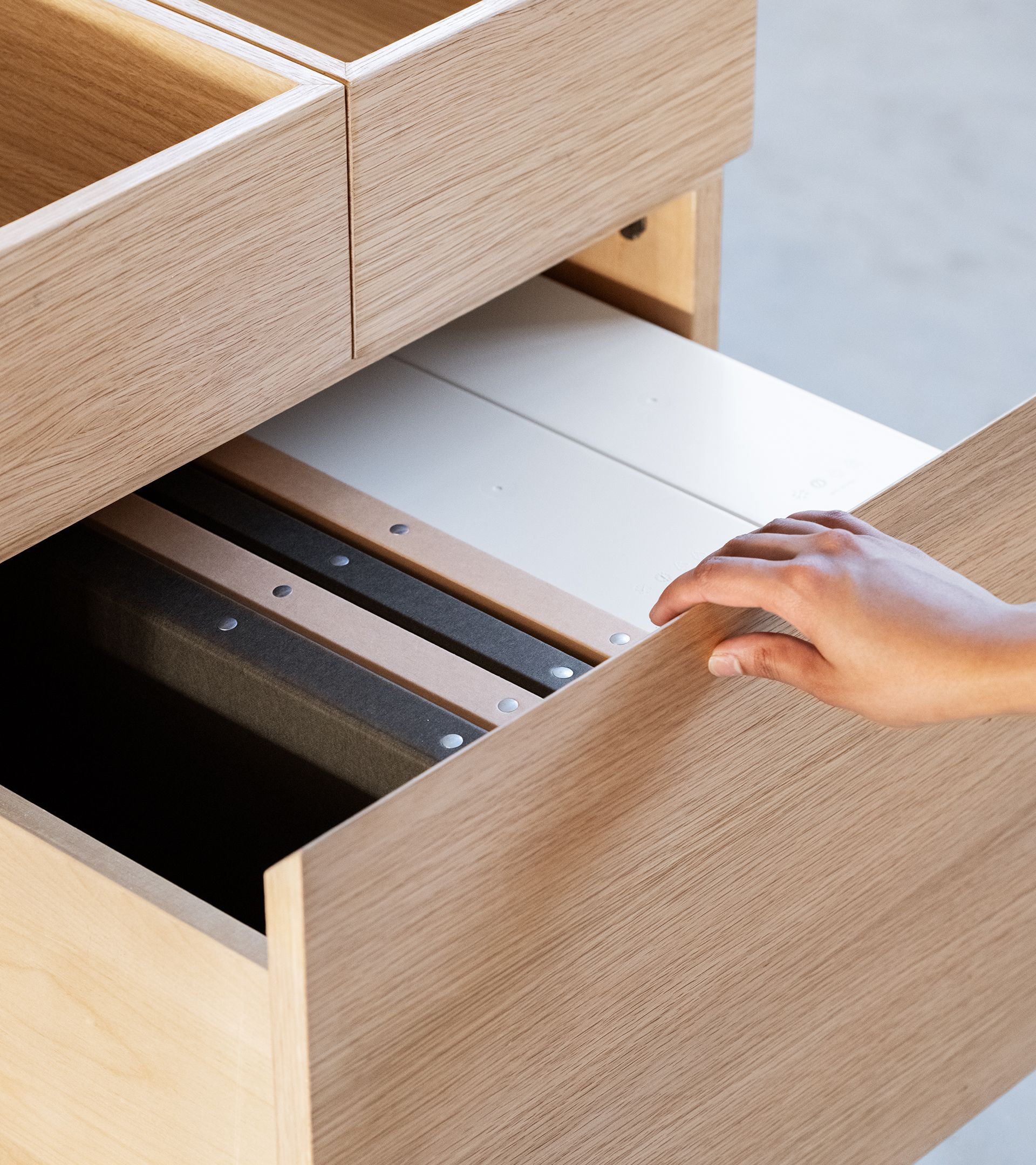 Hand pulling open white oak drawer revealing brand binders in black, tan, and white stacked in order