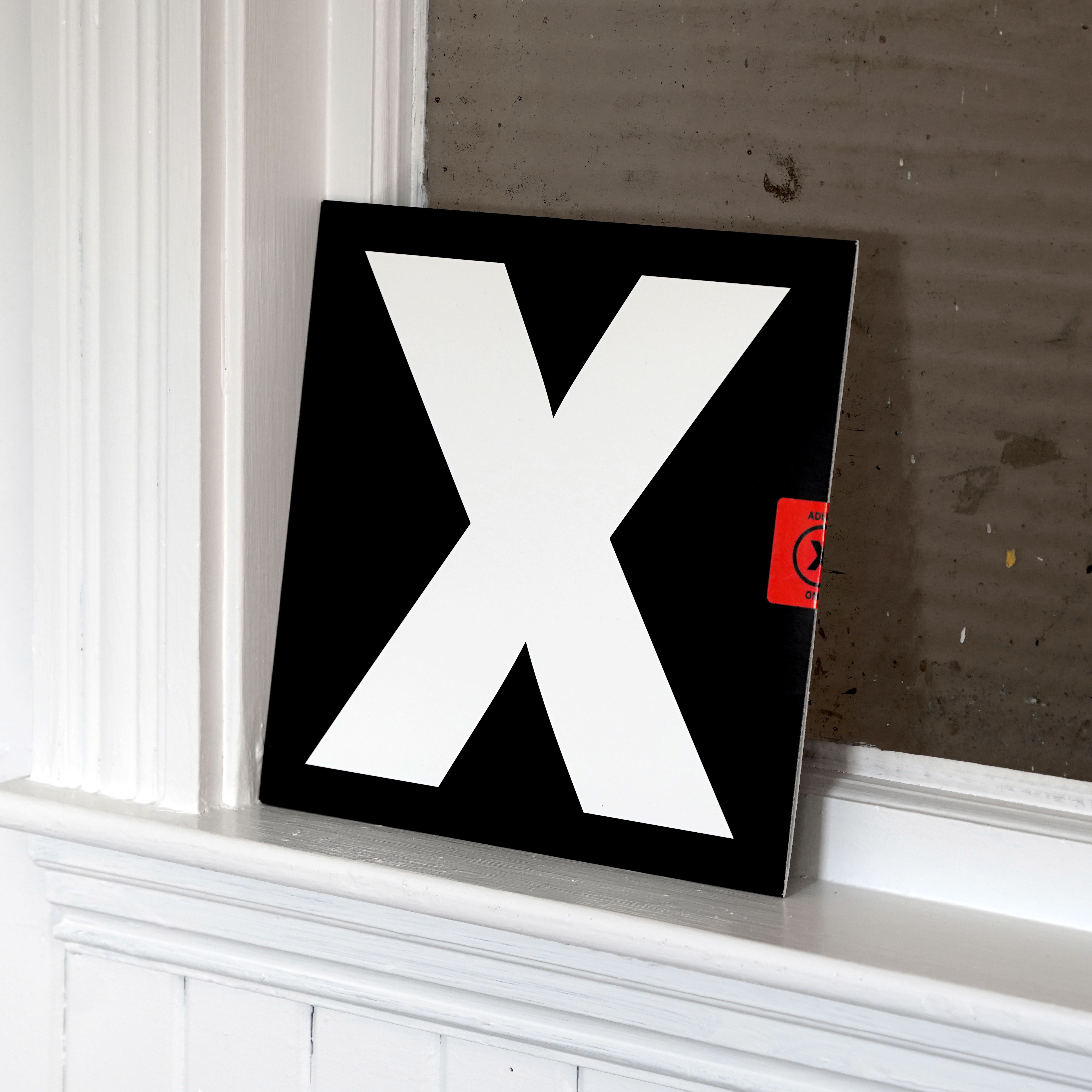 A24 X original soundtrack LP leaning on white mantle; oversized white X on black sleeve with red "Adults Only" sticker on edge