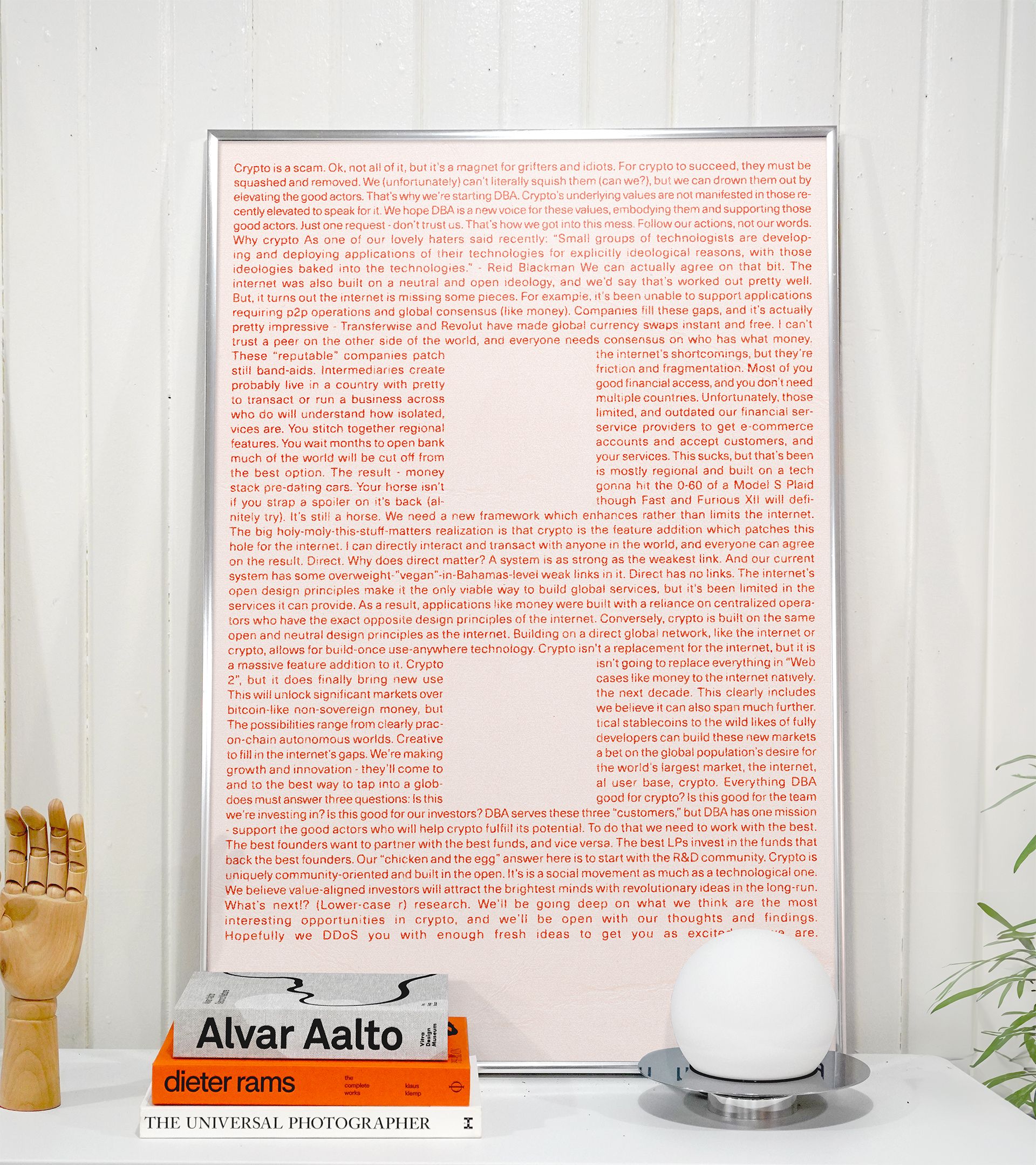 "Crypto is a scam..." manifesto text poster framed on wall propped against design books and lamp