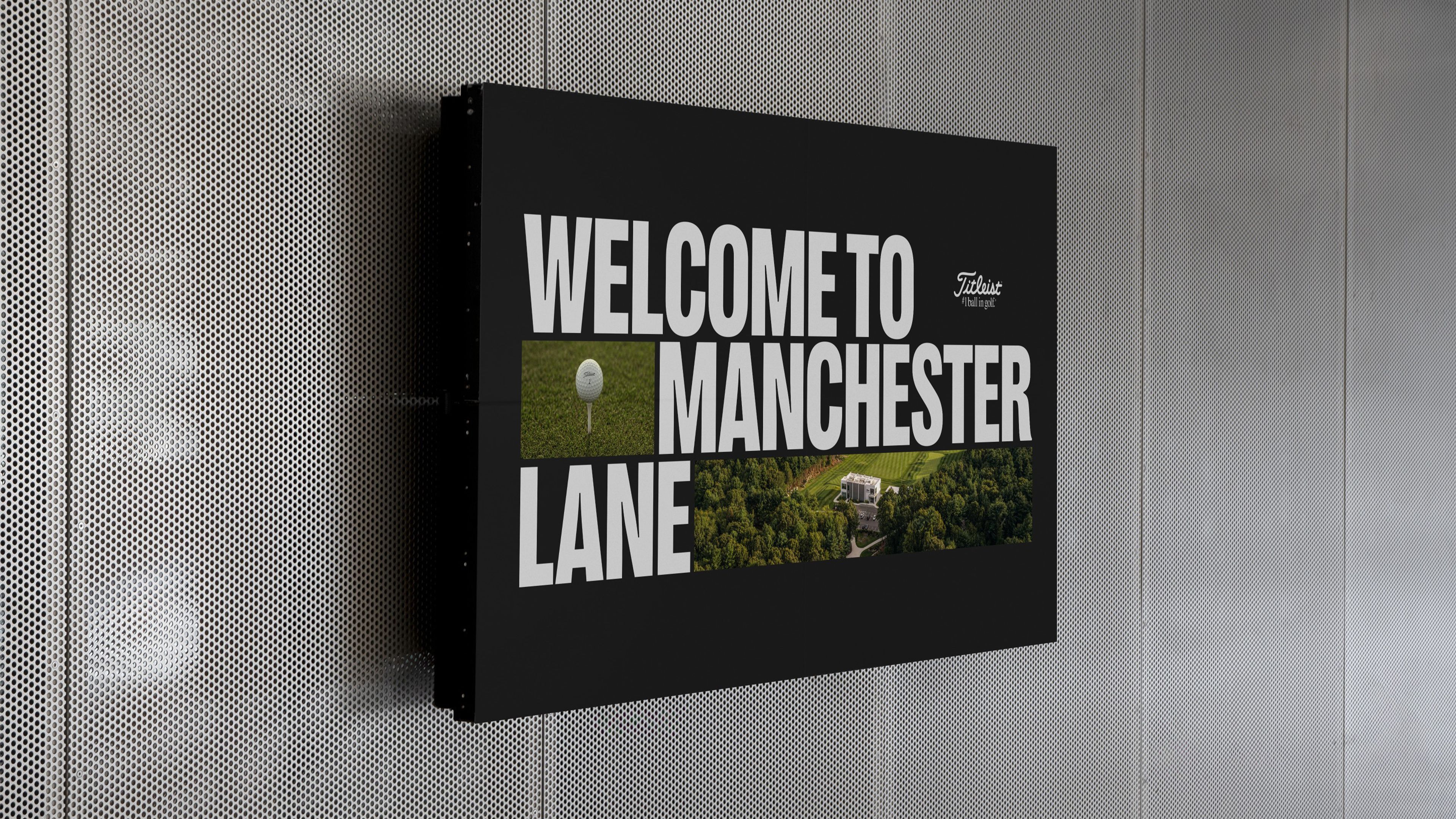 Wall-mounted black screen reading “Welcome to Manchester Lane” with a Titleist ball on a tee, an aerial view of a building among trees and a fairway, and the Titleist logo.