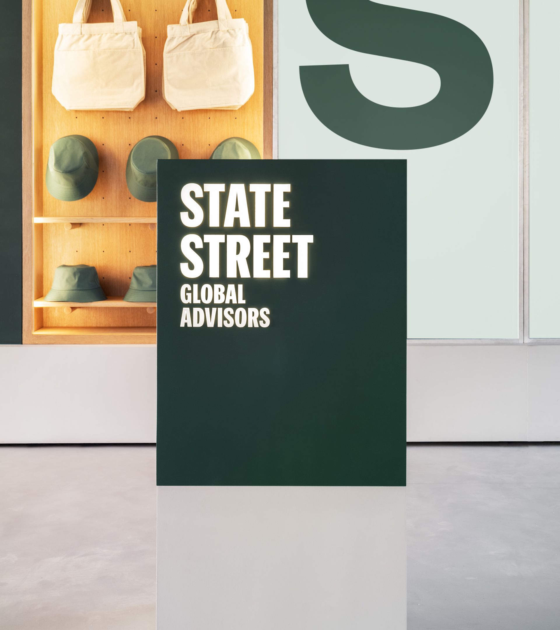 SSGA dark green podium with backlit wordmark; oak pegboard merch shelf and digital display in back showing SPY ticker