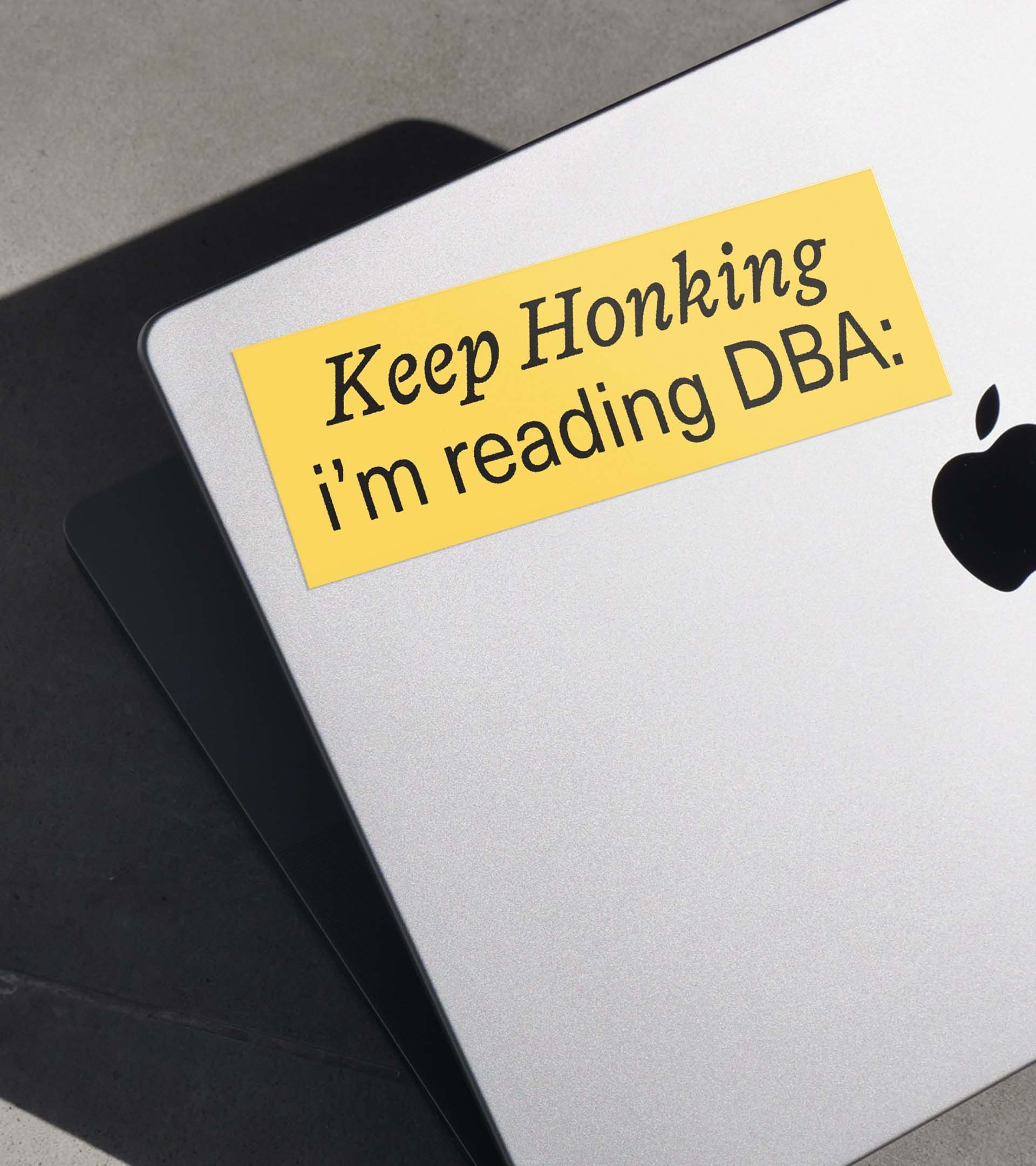 "Keep Honking i'm reading DBA:" yellow bumper sticker applied to MacBook