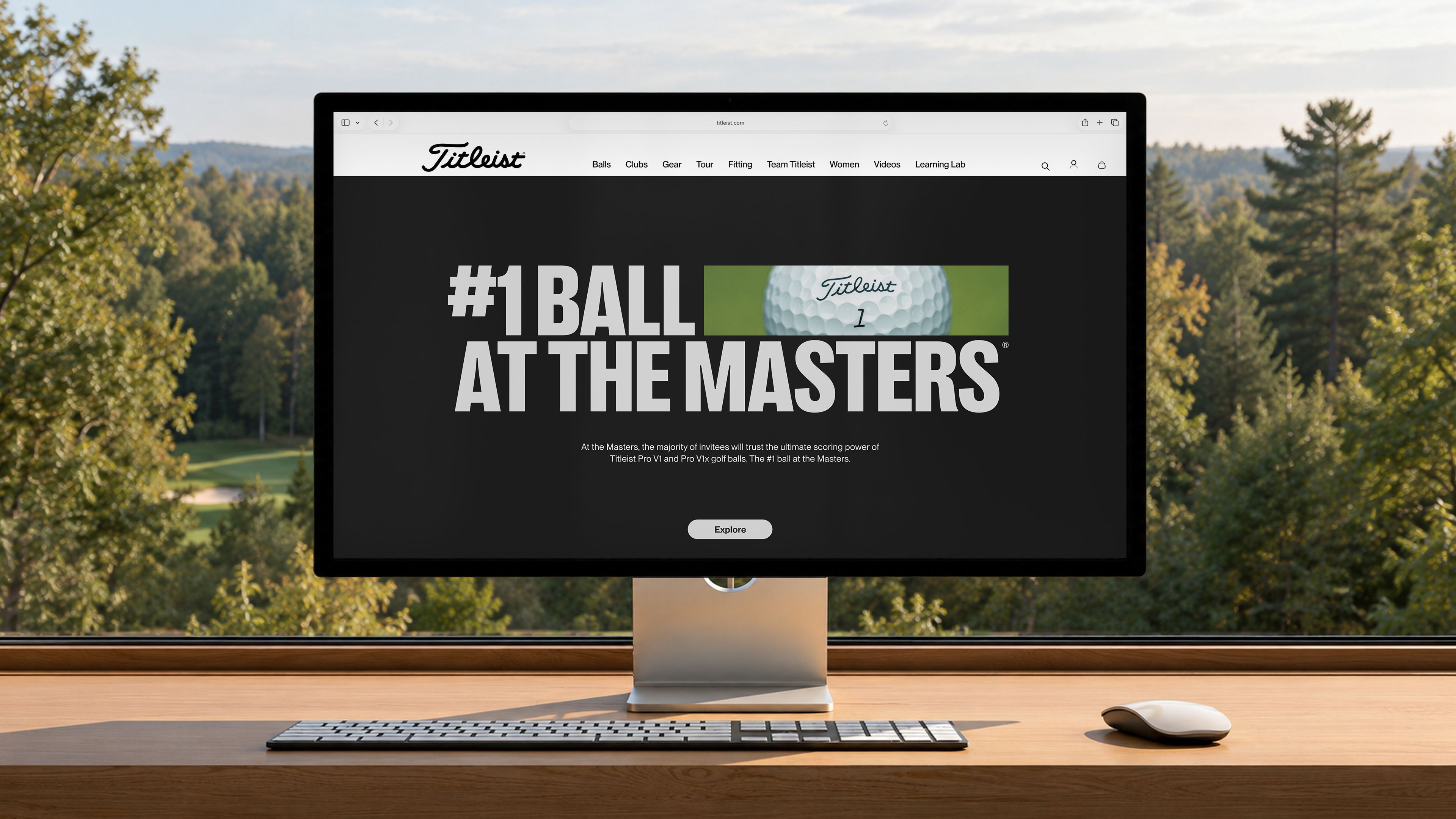 Monitor on a wooden desk showing the Titleist website with the headline “#1 Ball at the Masters” and an Explore button, with a wooded golf course outside the window.