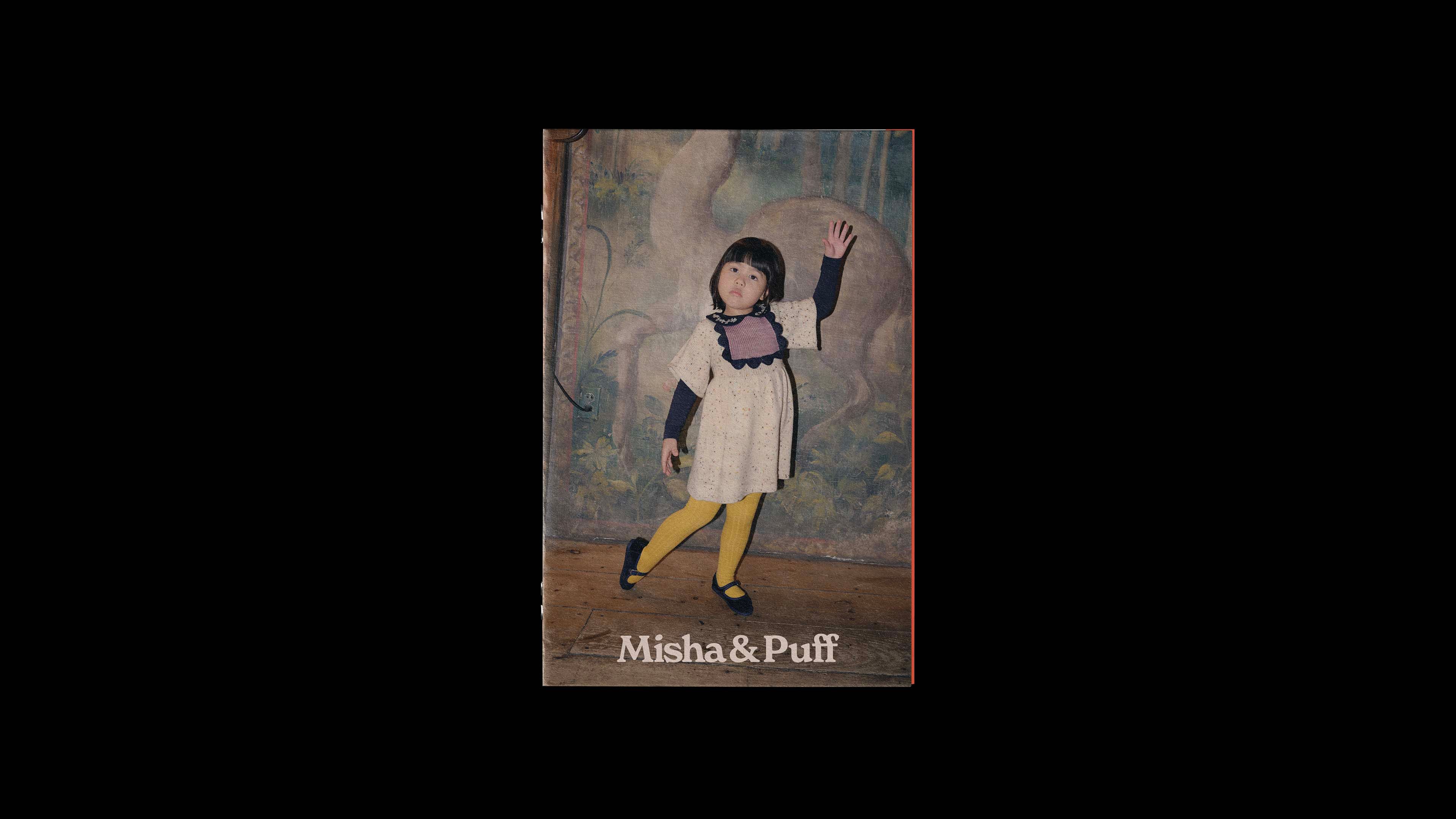 Misha & Puff catalog cover: child in a white dress with scalloped bib waves in front of a tapestry. Brand name below image.