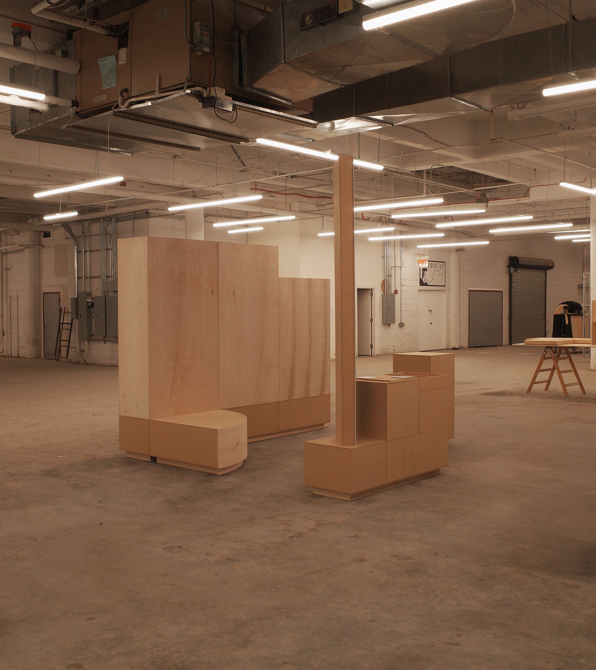Natural birch plywood exhibition booth components in empty industrial warehouse — full build in progress