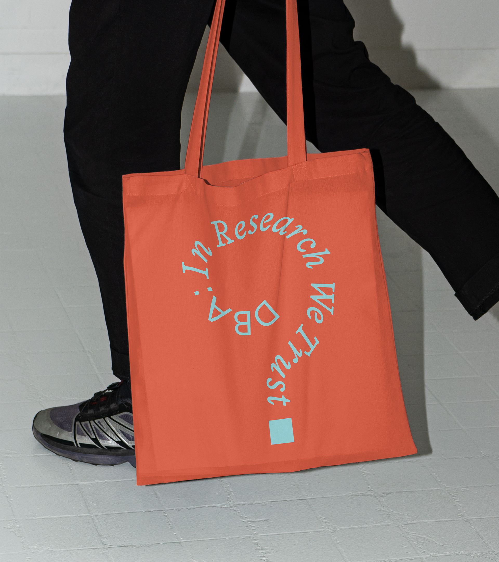 Orange tote with "In Research We Trust / DBA:" in cyan curving into question mark brand motif