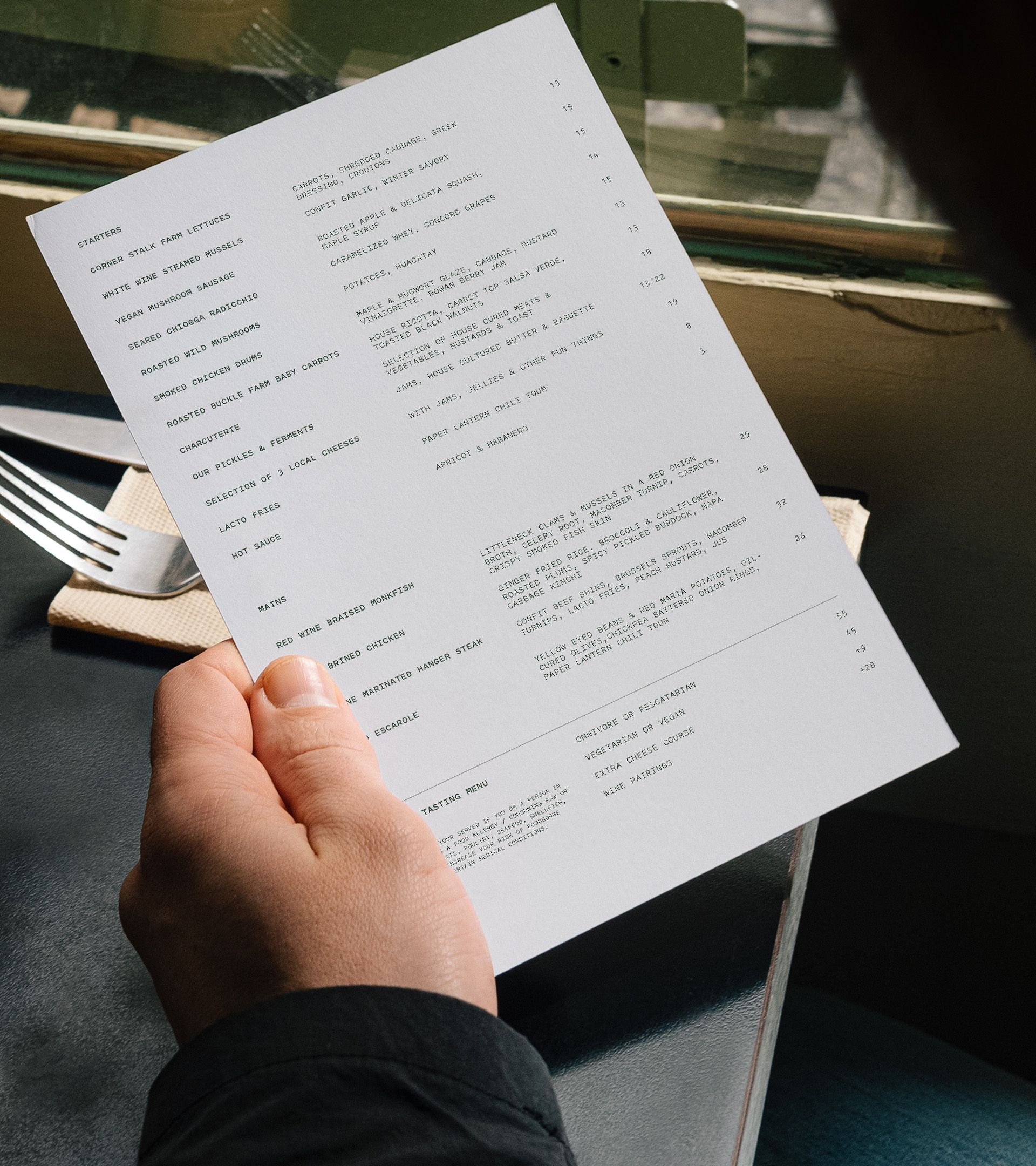 Forage menu: hand holding single typewritten sheet at outdoor table with table setting below