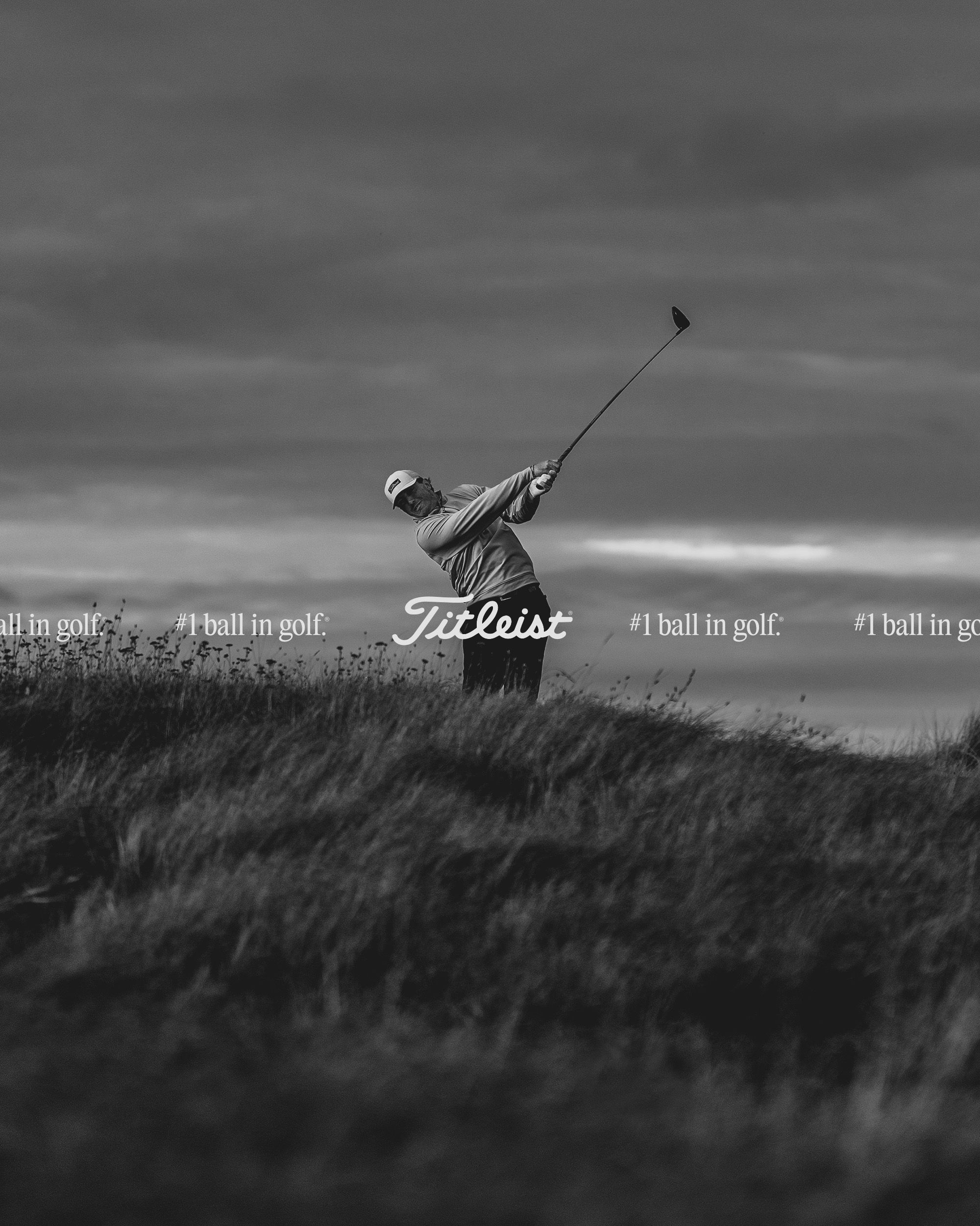 Golfer mid-swing on a links course, dramatic overcast sky, Titleist script and "#1 ball in golf." overlaid as a horizontal ticker