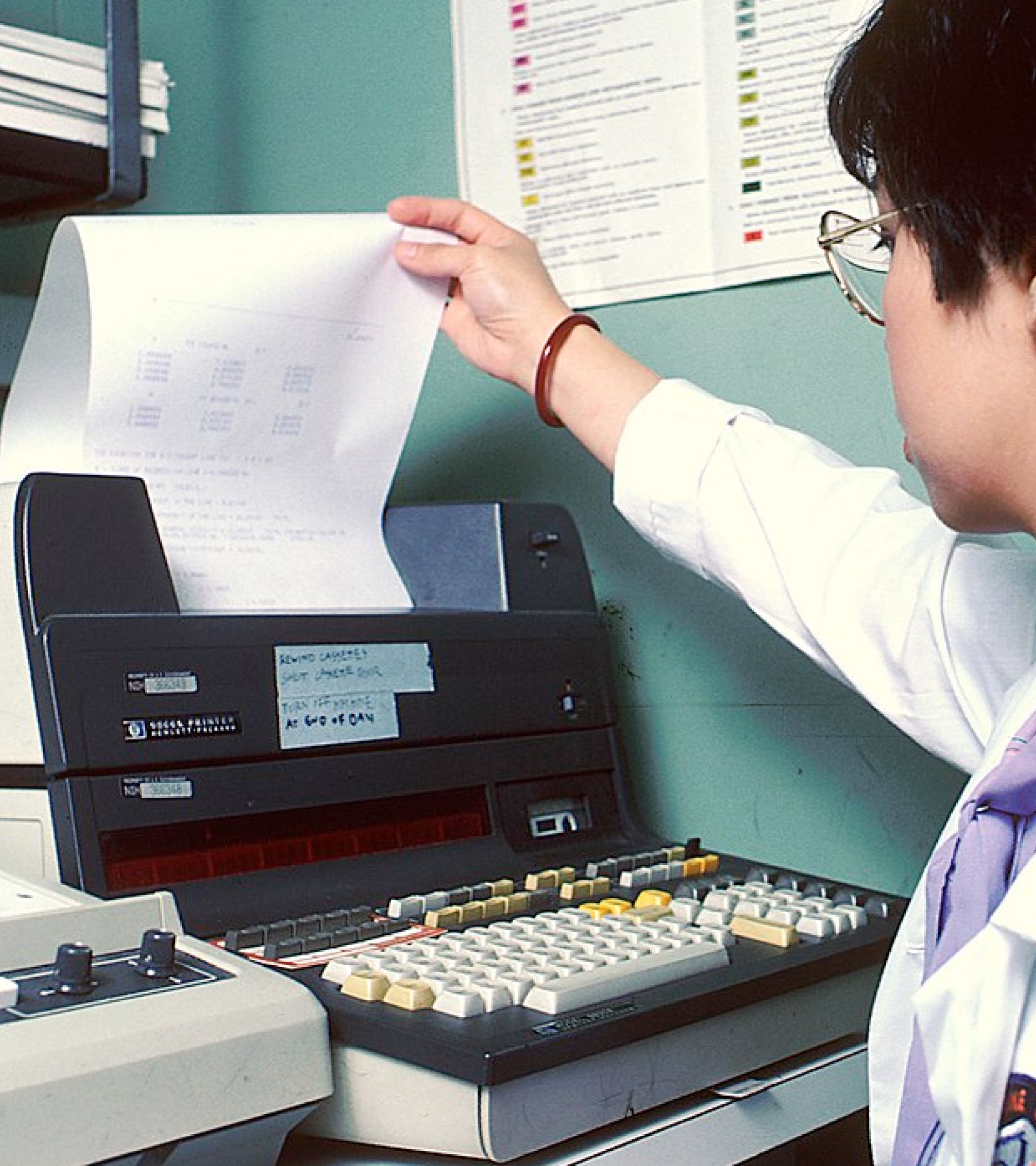 Person in lab coat pulling printout from vintage HP matrix printer — archival editorial photo