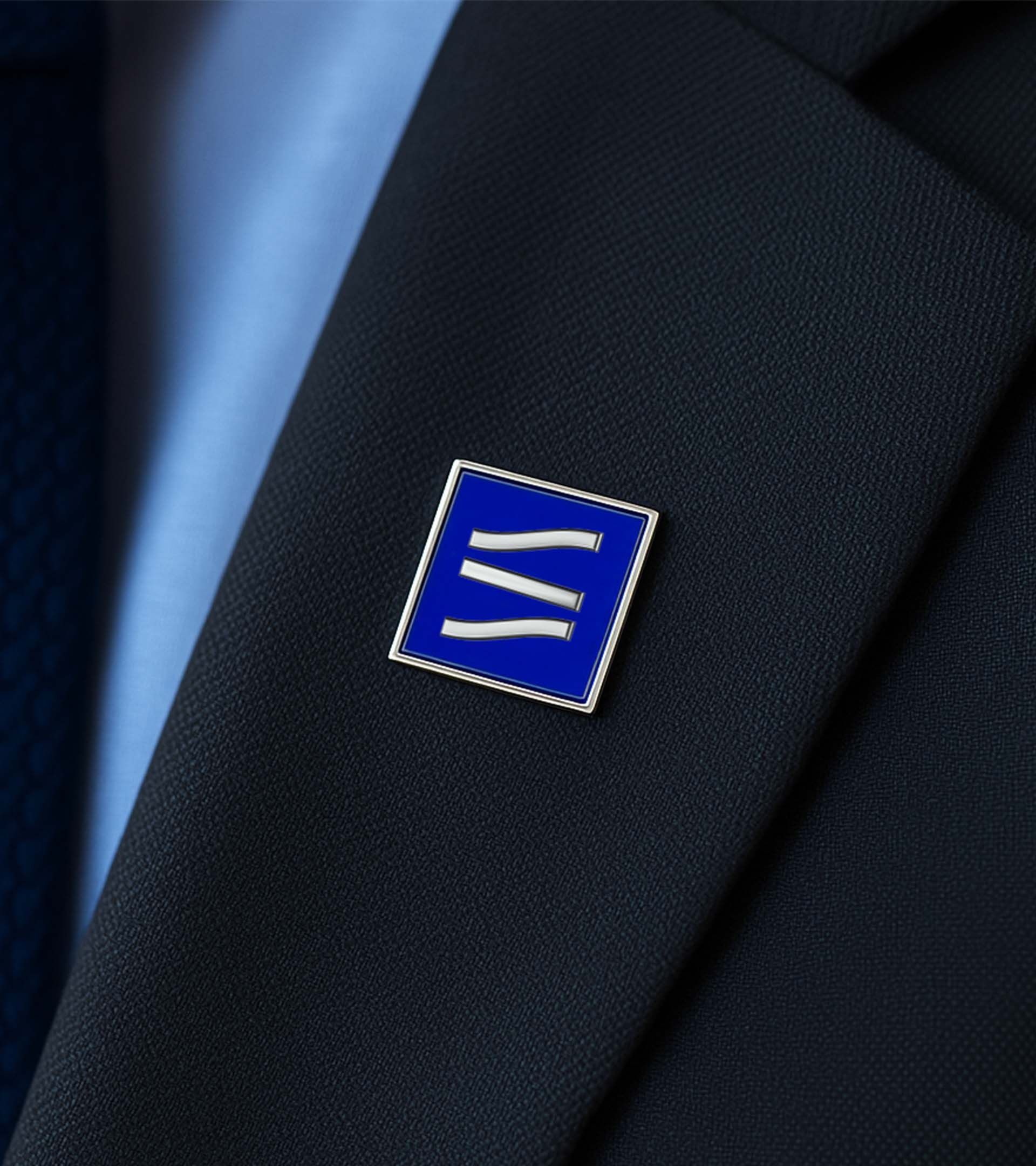 Close-up of navy suit lapel with square blue enamel pin featuring the State Street wave mark in white