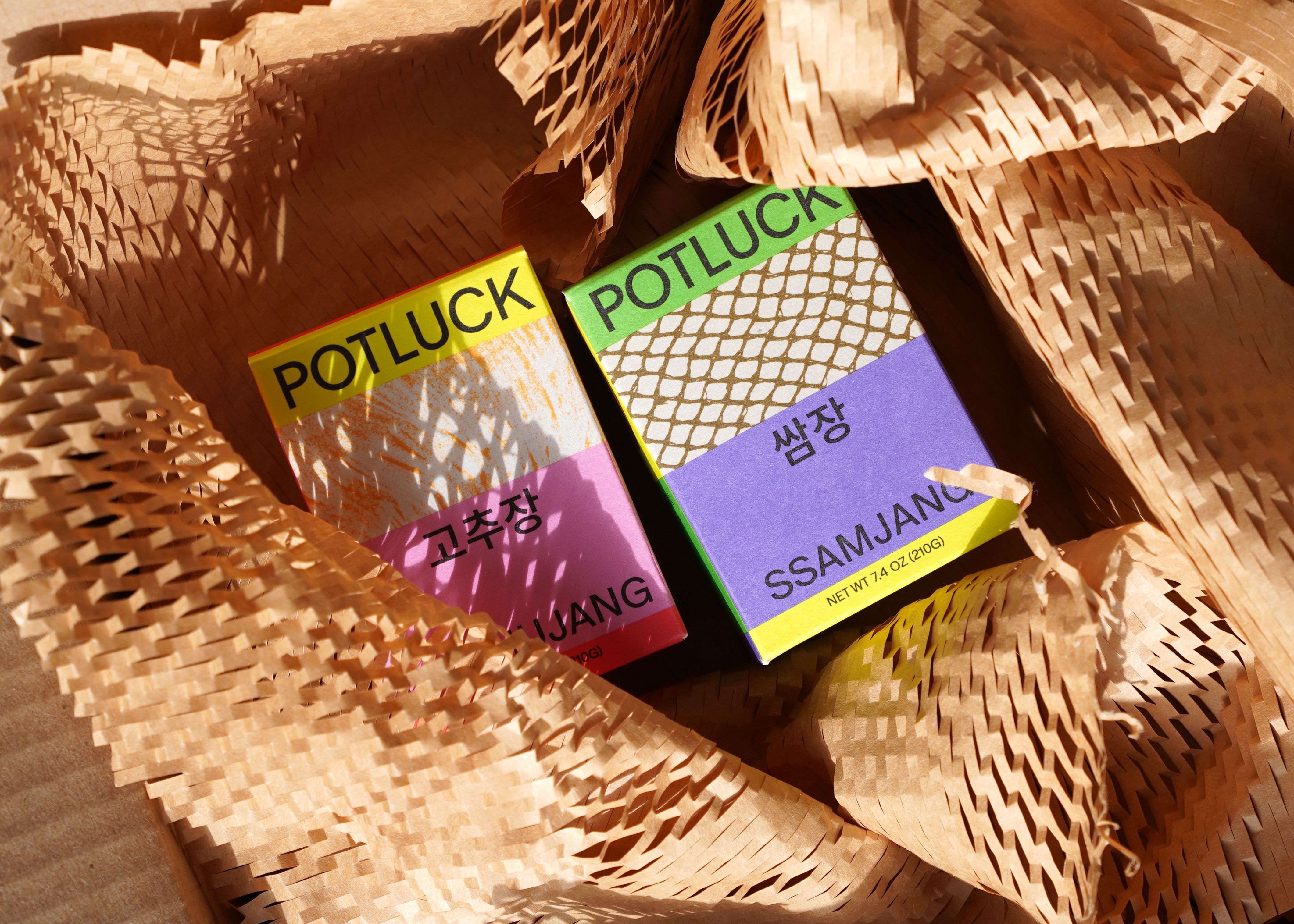 Two boxes, Gochujang and Ssamjang, in neon yellow, pink, green, and purple on honeycomb kraft paper in sunlight
