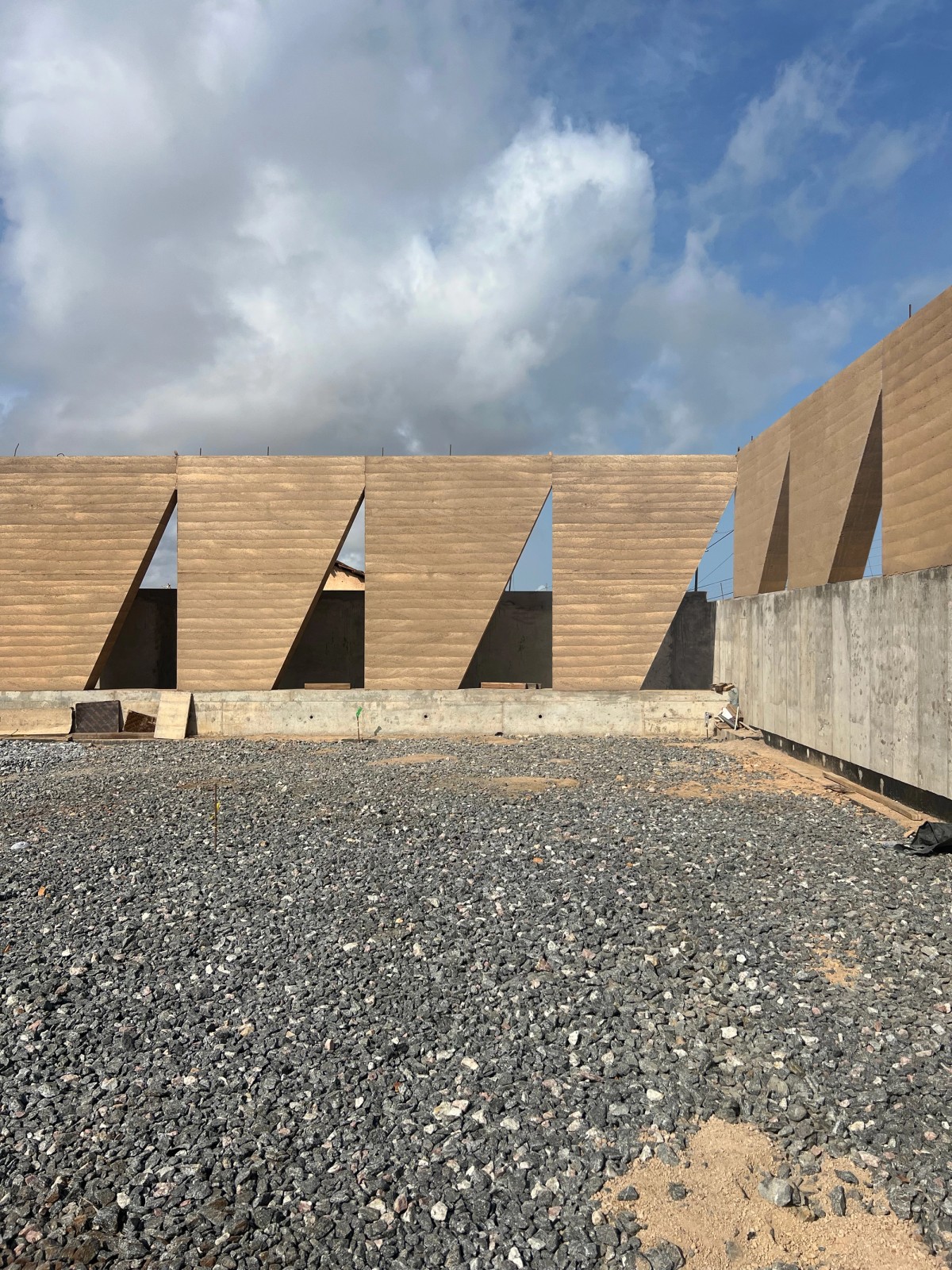 Giant rammed walls stand in front of a cloudy sky, the spaces in between creating geometric patterns