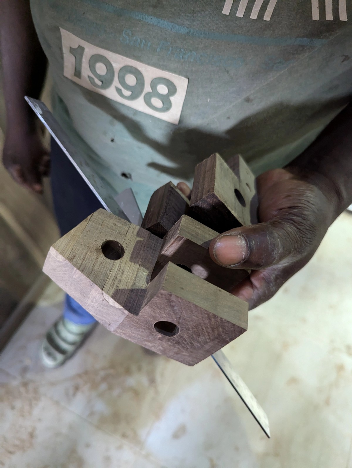 Wooden blocks grapsed by a hand of a figure who is wearing a shirt that says "1998"