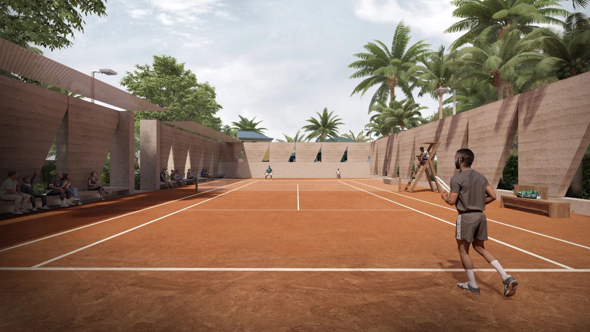 A clay tennis court is surrounded by textured earthen walls with geometric cutouts and shaded seating areas, where spectators watch the match. Palm trees rise above the walls, creating a tropical backdrop as players engage in an active game under a bright sky.