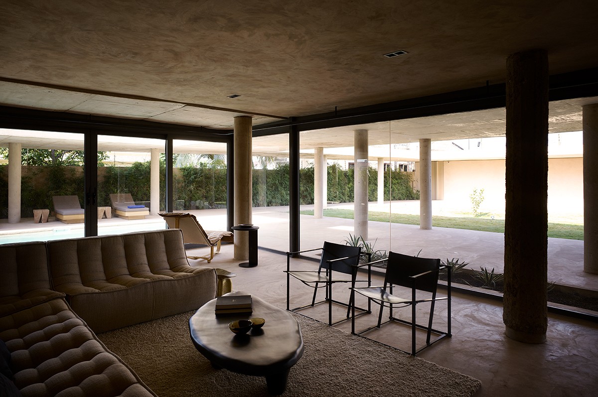 A spacious, modern living room with floor-to-ceiling glass walls opens onto a covered patio and landscaped courtyard
