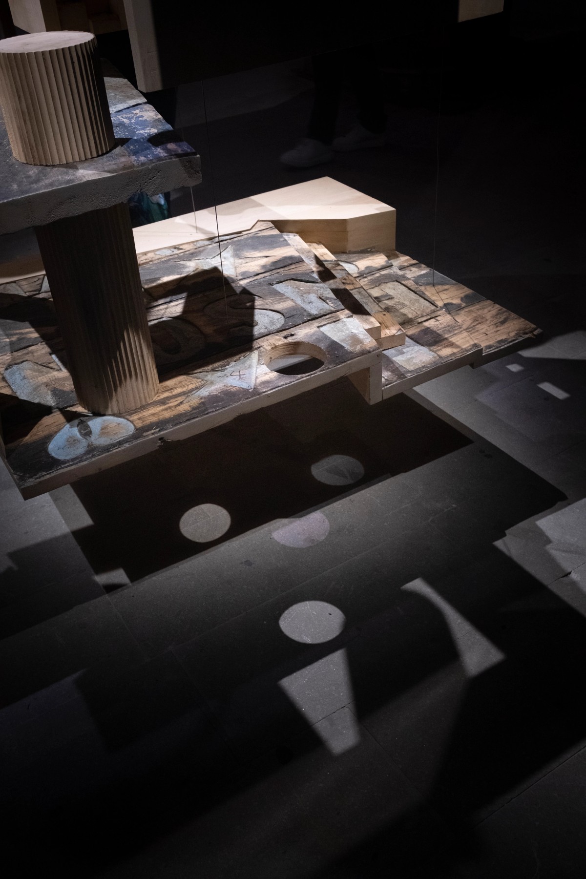 Close-up of a suspended architectural sculpture’s base made from painted, reclaimed wood with abstract patterns.