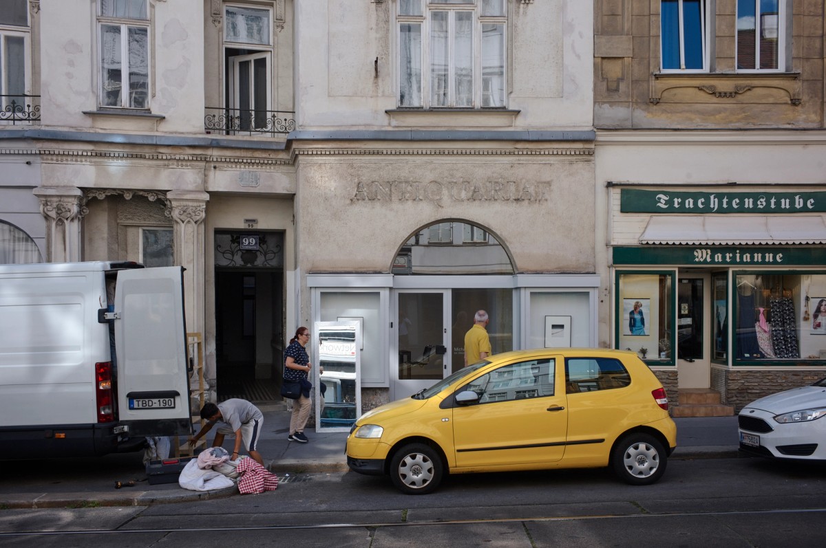 ehicles including a bright yellow car are parked in front of three buildings connected to each other